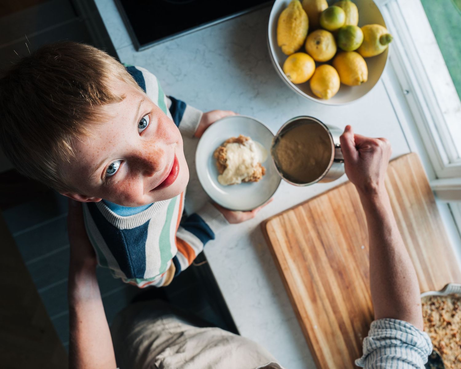 small boy looking up at the camera smiling holding homemade apple crumble and custard for a commercial food photographer shoot in Stockholm