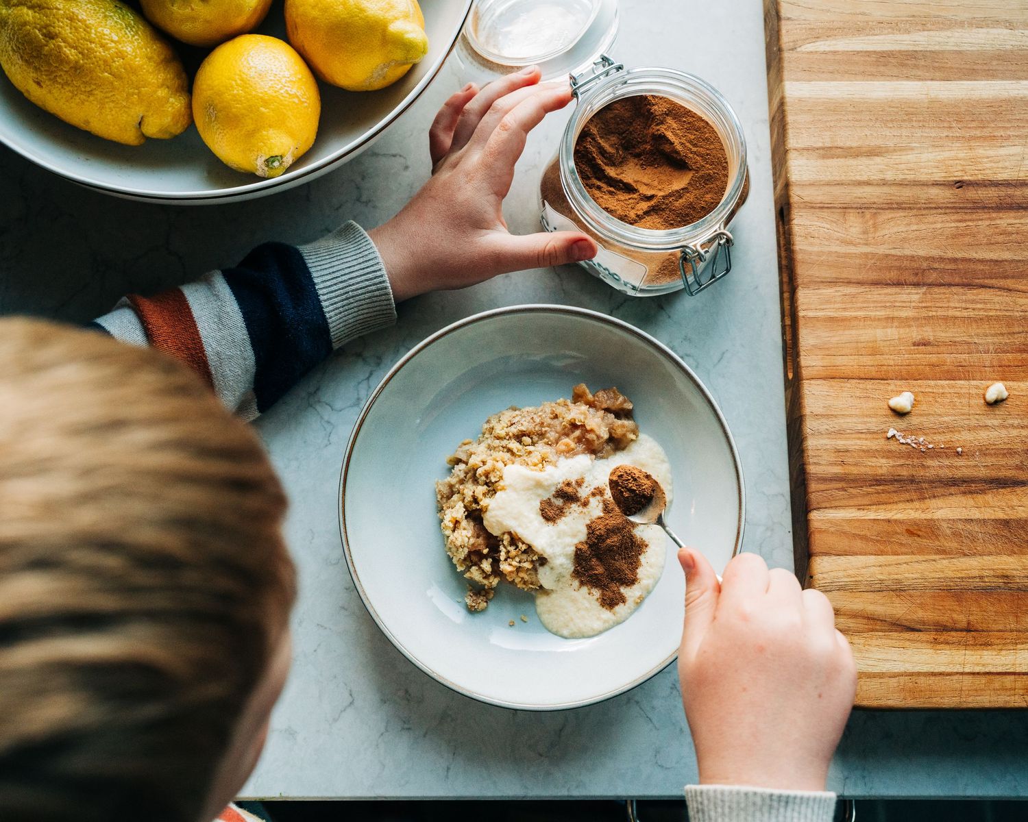 boy sprinkling cinnamon on his apple crumble with custard. A commercial photography shoot for a cook book. mat och drykerfotografering
