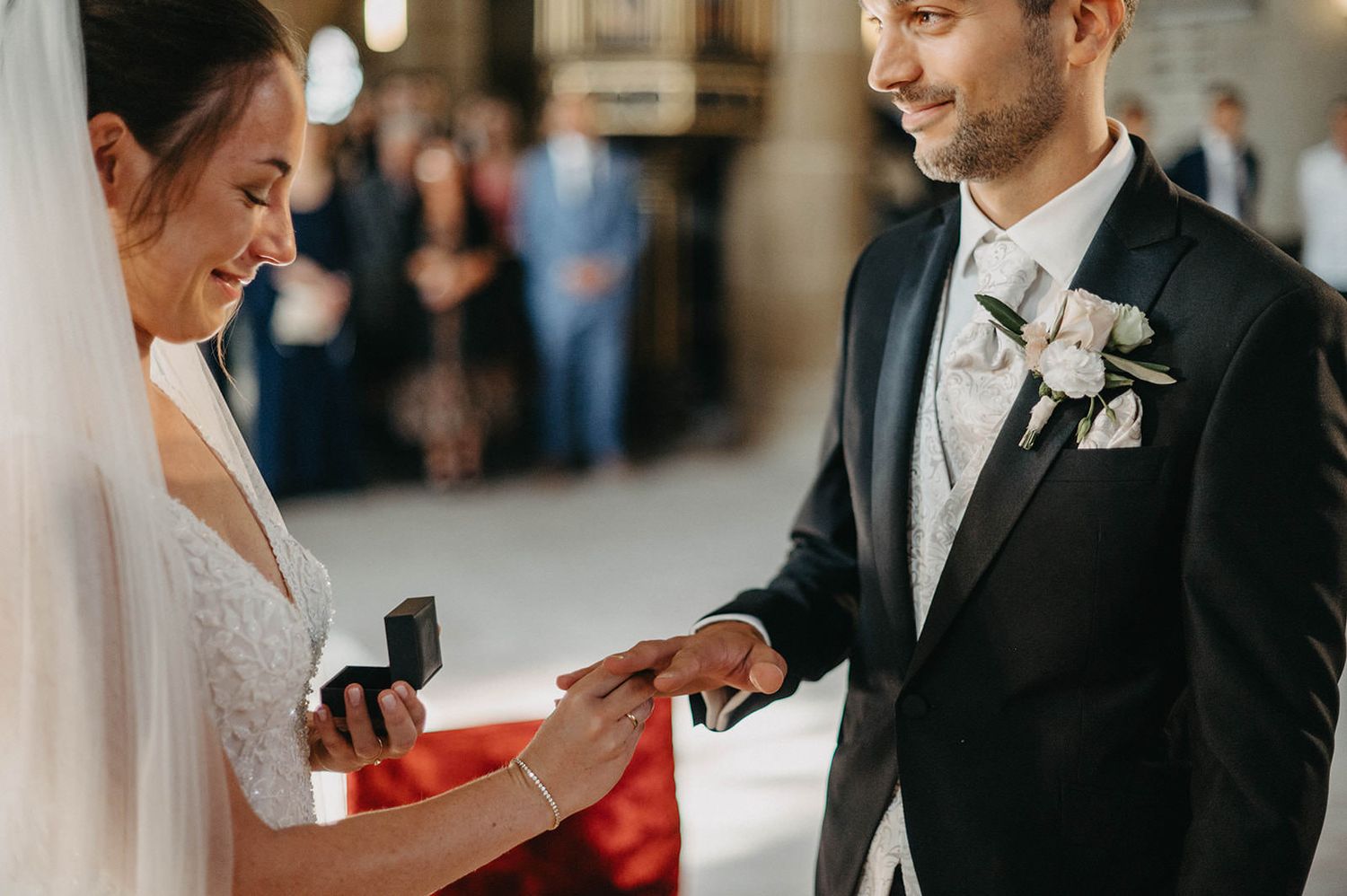 A couple exchanges rings during an elegant church wedding ceremony with guests watching in the background.