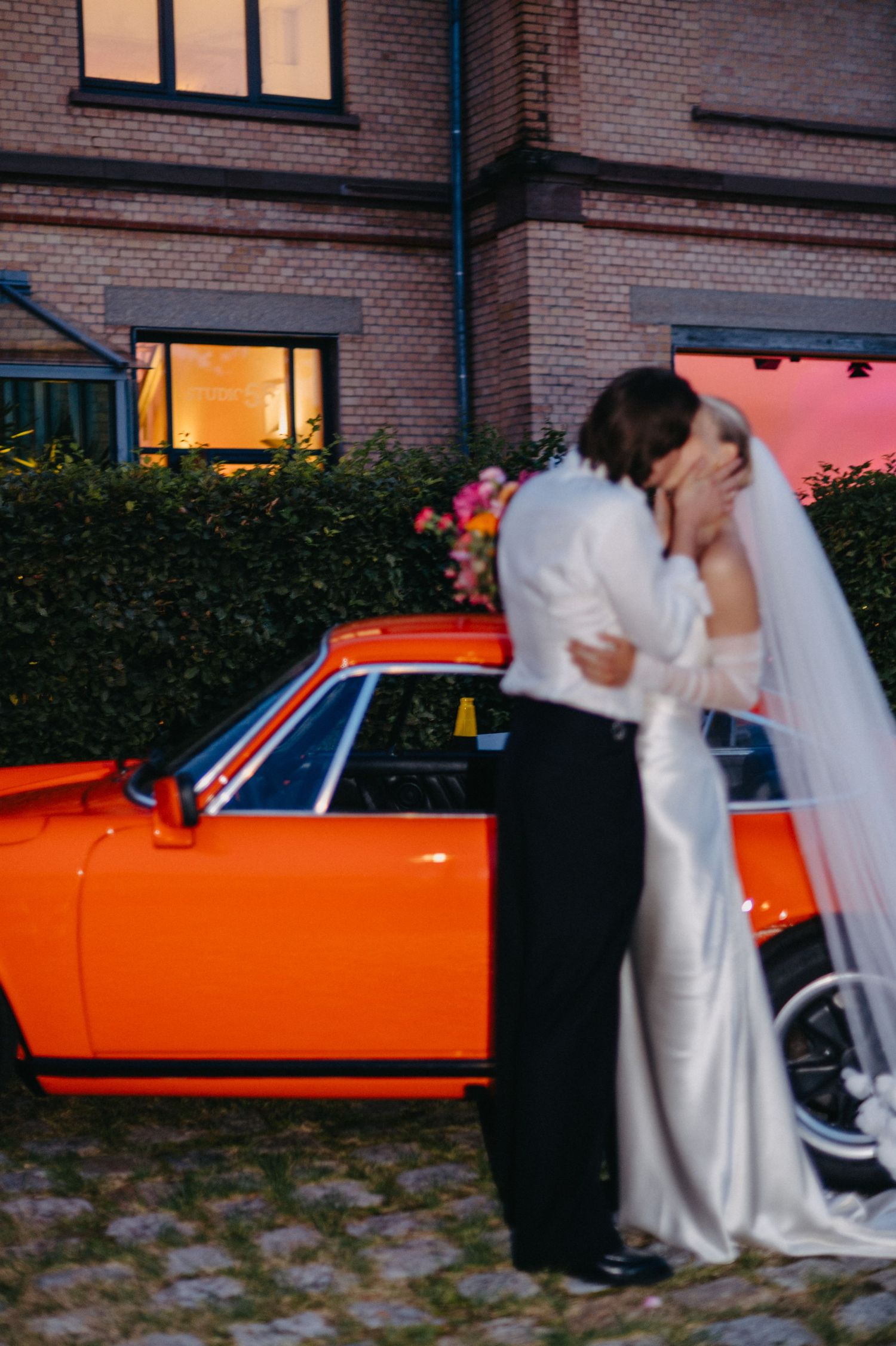 A series of romantic wedding photos showing a couple by a vintage orange car at dusk.