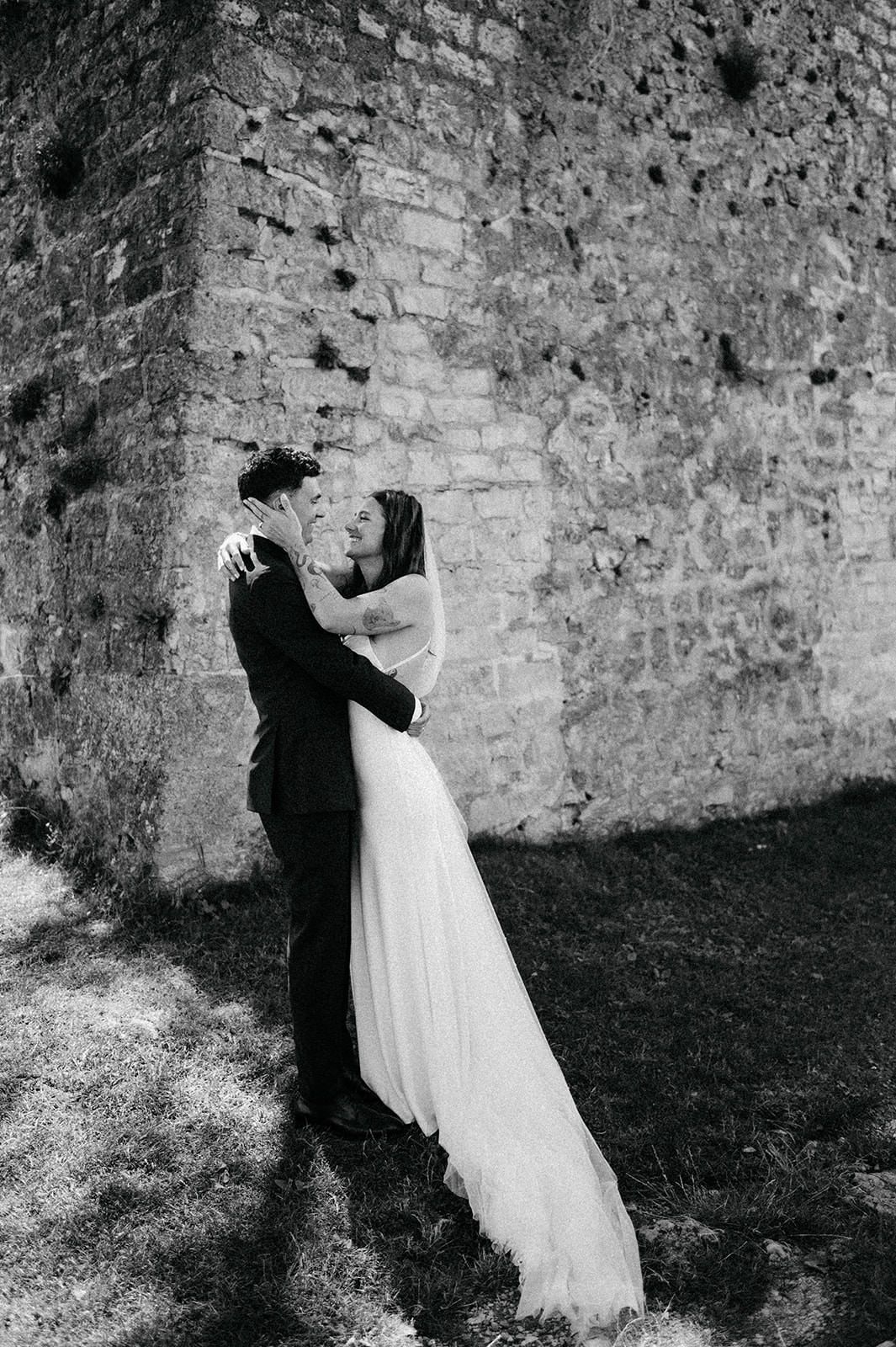 A sequence of black and white photos showing a couple in wedding attire dancing against a stone wall.