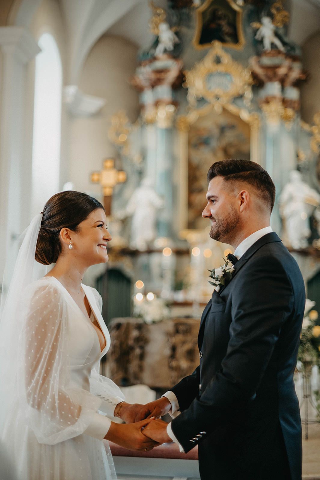 A romantic wedding ceremony unfolds in an ornate church with gilded decorations and religious statues.