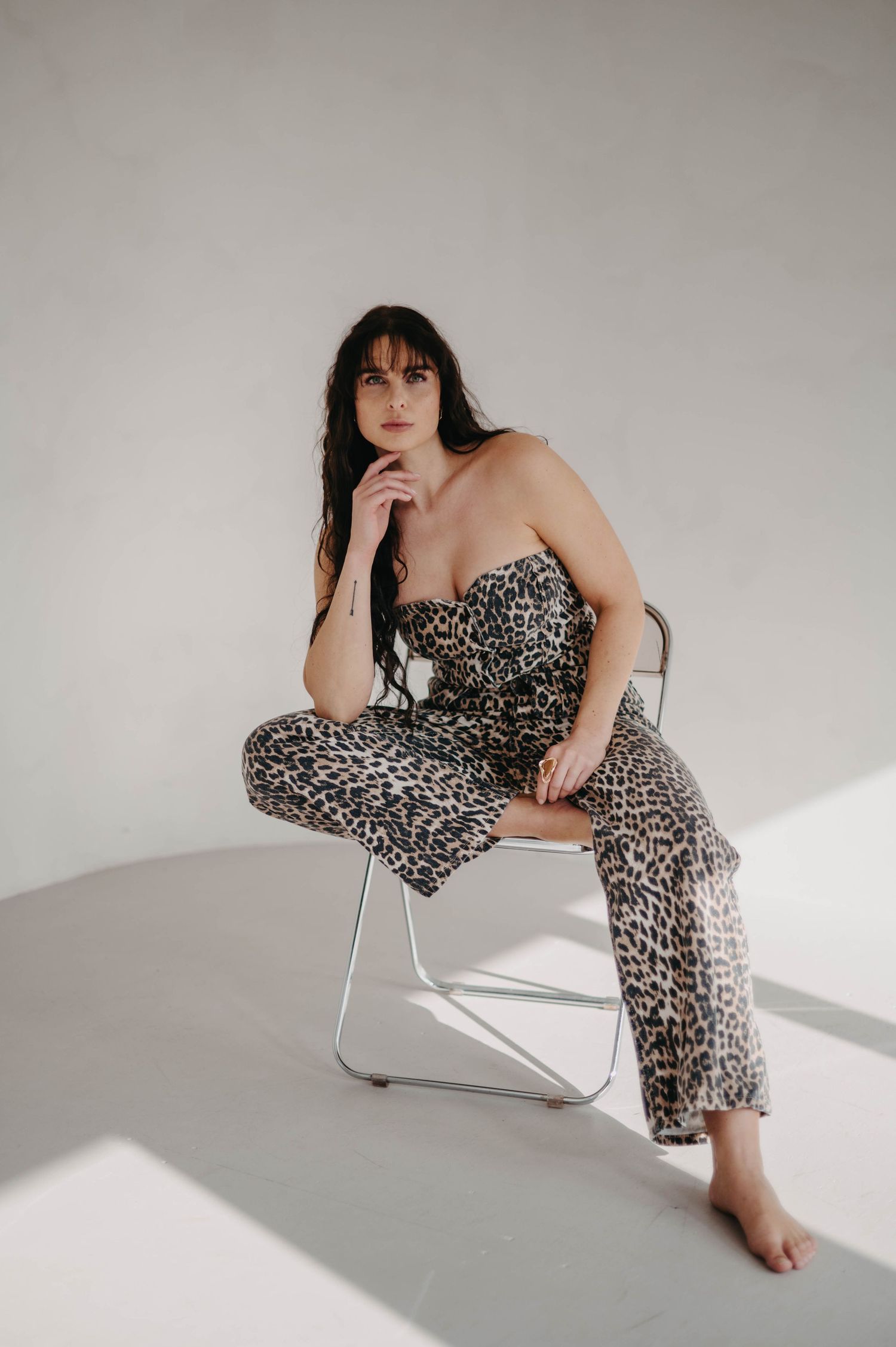 Person in leopard print outfit poses thoughtfully on modern white chair.