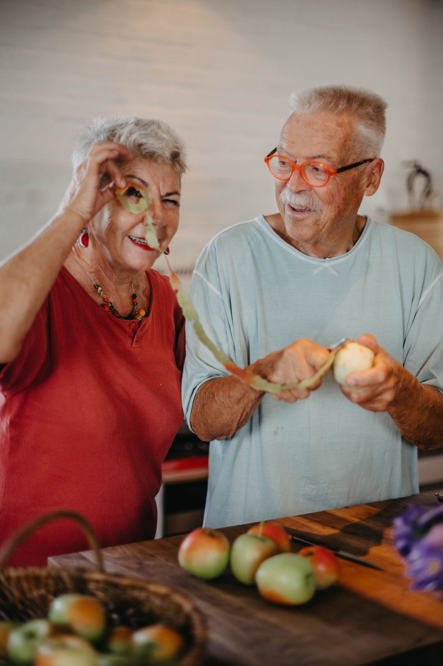 Senior couple laughing while preparing food together in kitchen with fresh produce.