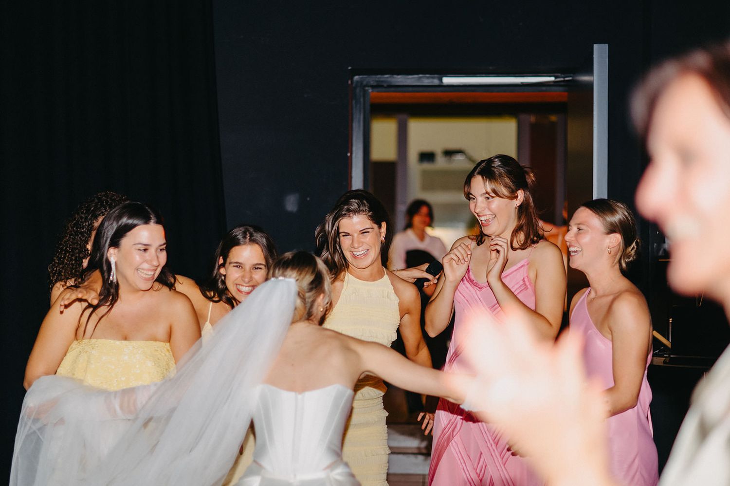Wedding party members in pink and yellow bridesmaid dresses gather together on the dance floor during reception.