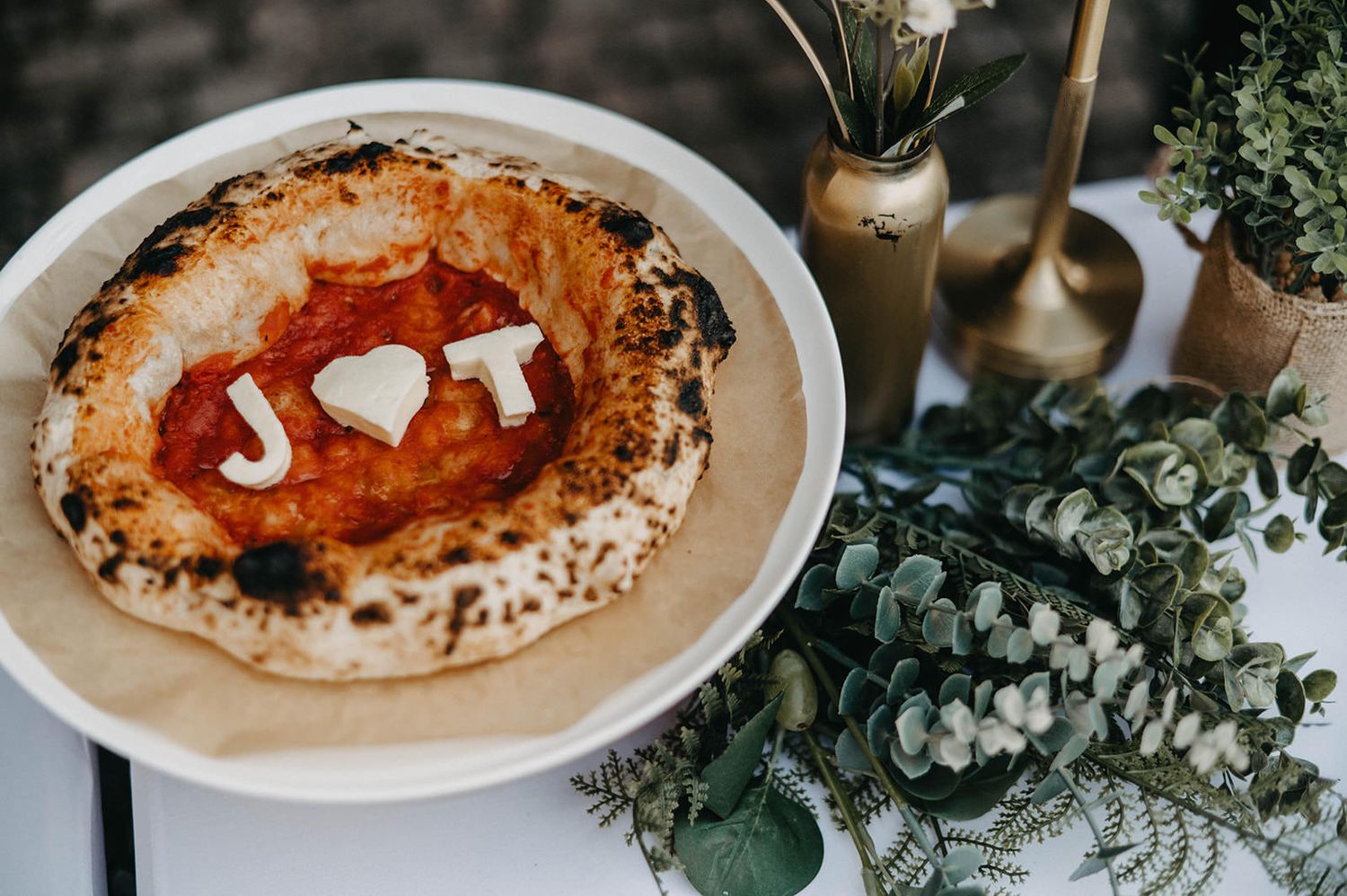 A series of hummus bowls with various toppings and garnishes arranged on a rustic table with eucalyptus branches.