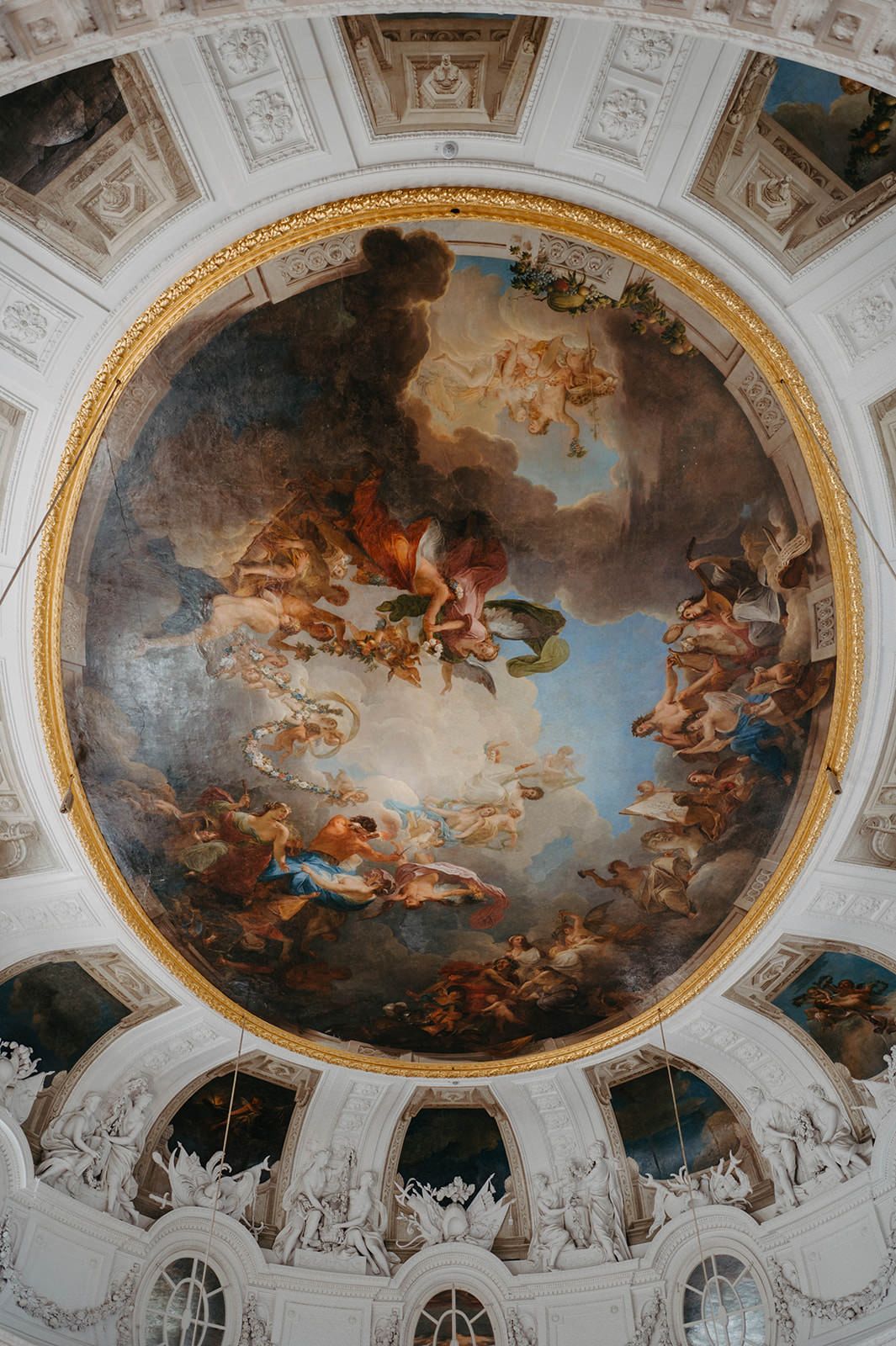 Ornate baroque ceiling fresco paintings with cherubs and religious figures in an oval dome surrounded by gilded architecture.