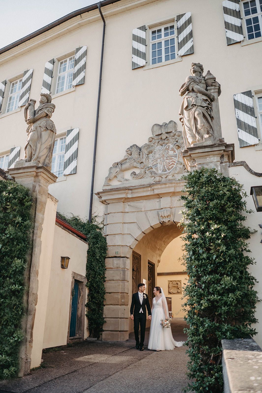 Ornate stone archway entrance with statues adorning the top at a historic European building with white walls and windows.