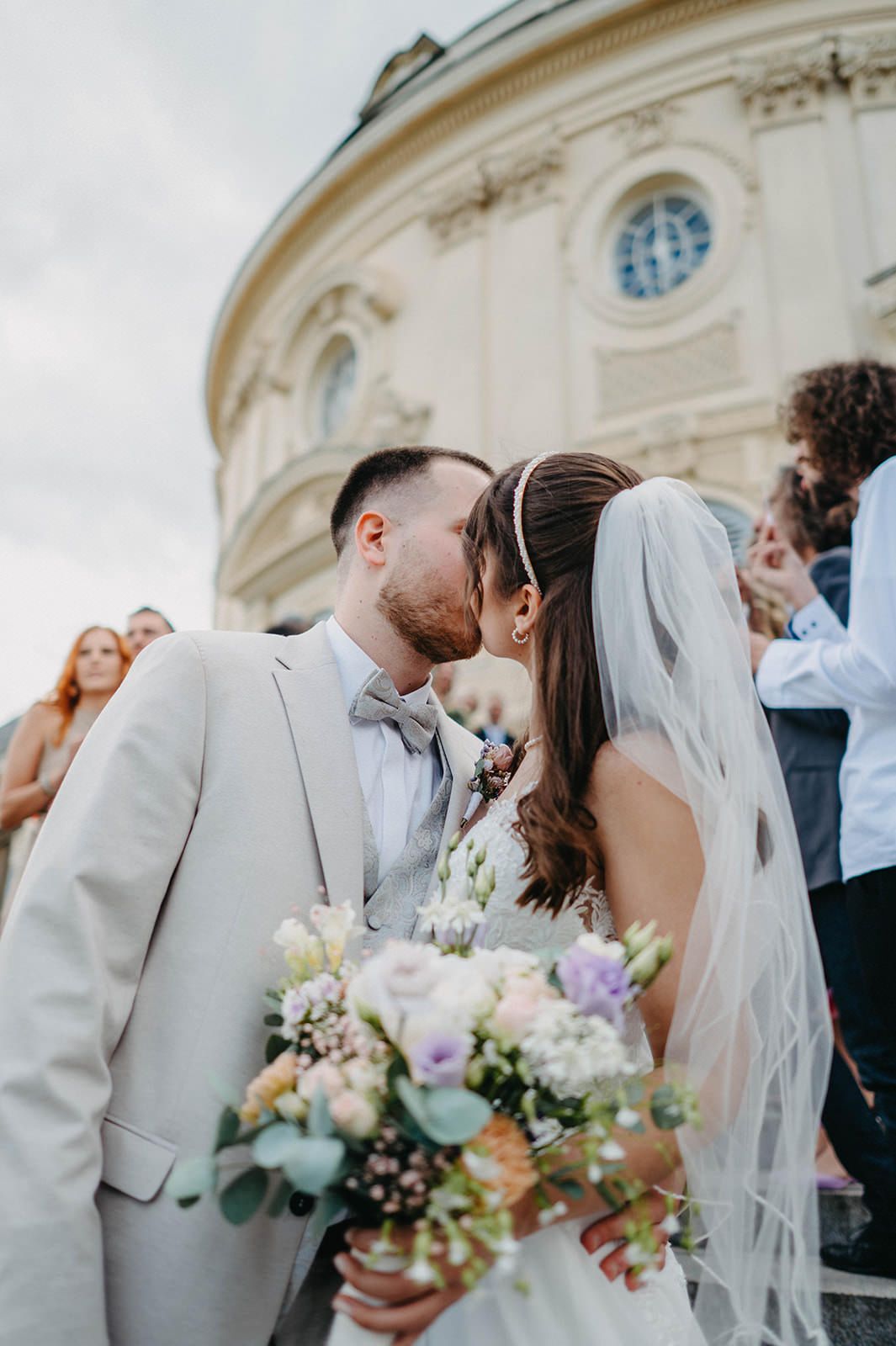 A romantic wedding moment outside a historic building with a beautiful bouquet of pastel flowers and flowing veil.