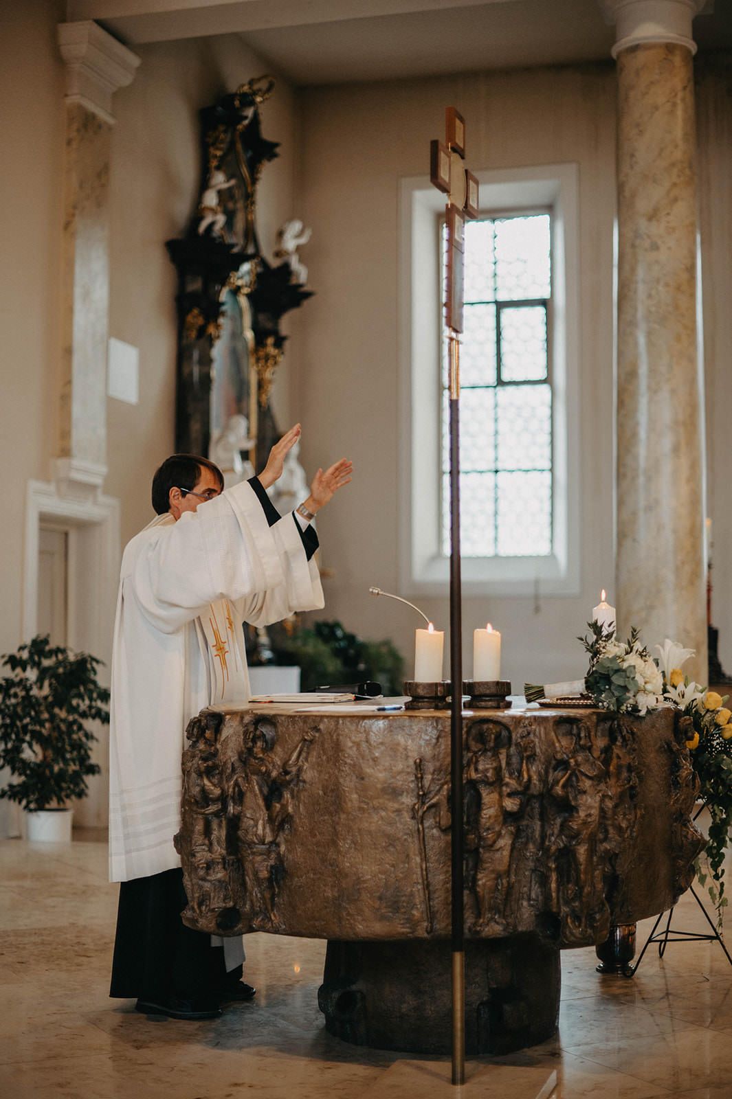 Rustic wooden altar decorated with white candles and greenery in a minimalist white interior space.