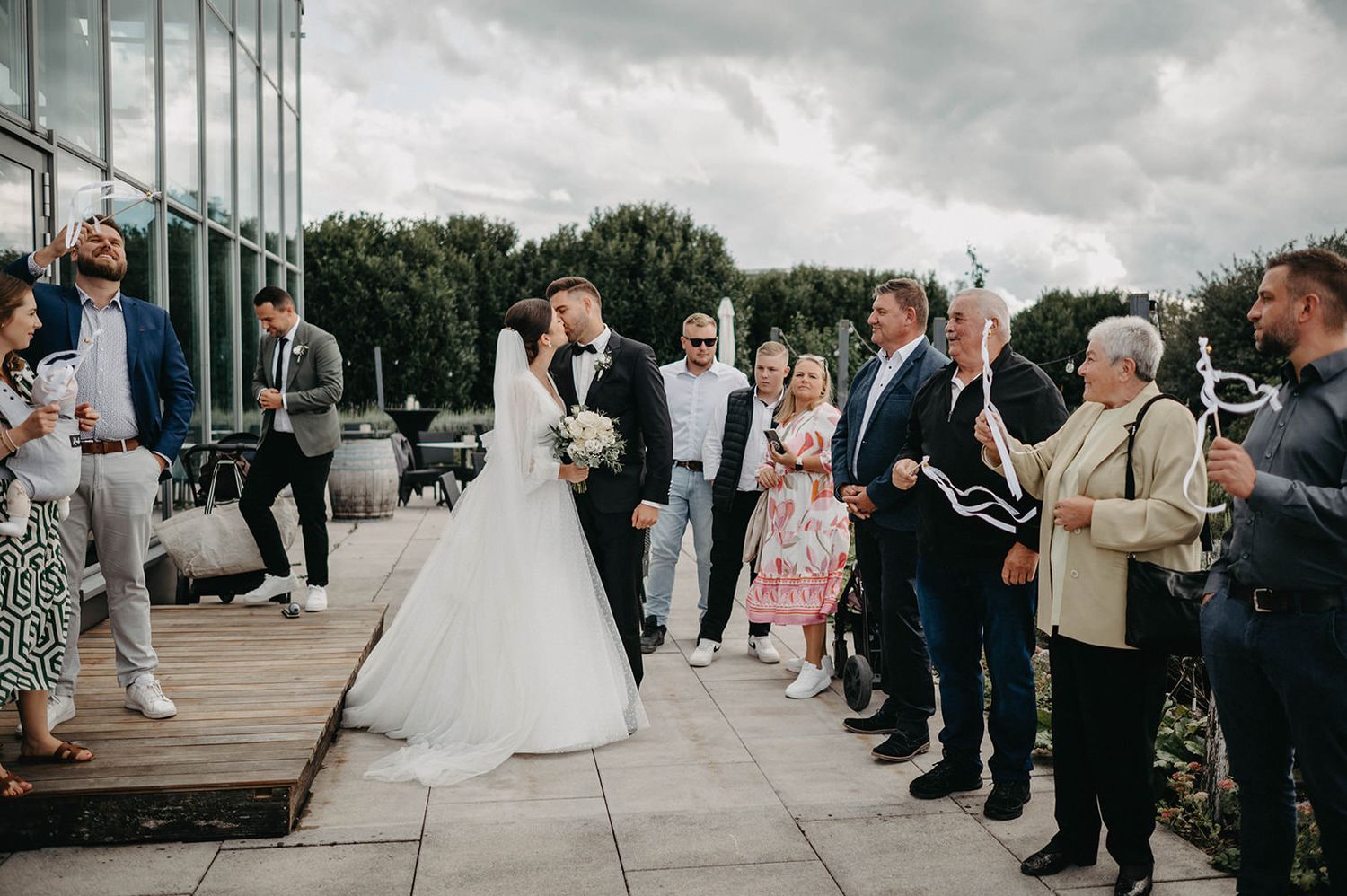 Wedding party and guests gather outside a modern building for post-ceremony celebrations.