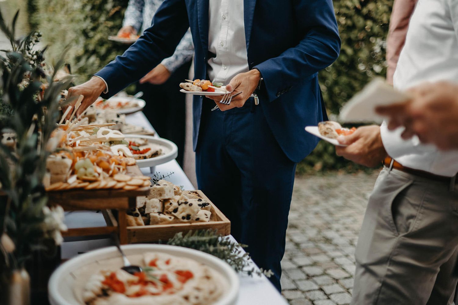 Close-up view of hands serving appetizers at an elegant outdoor catering event with plates of gourmet finger foods.