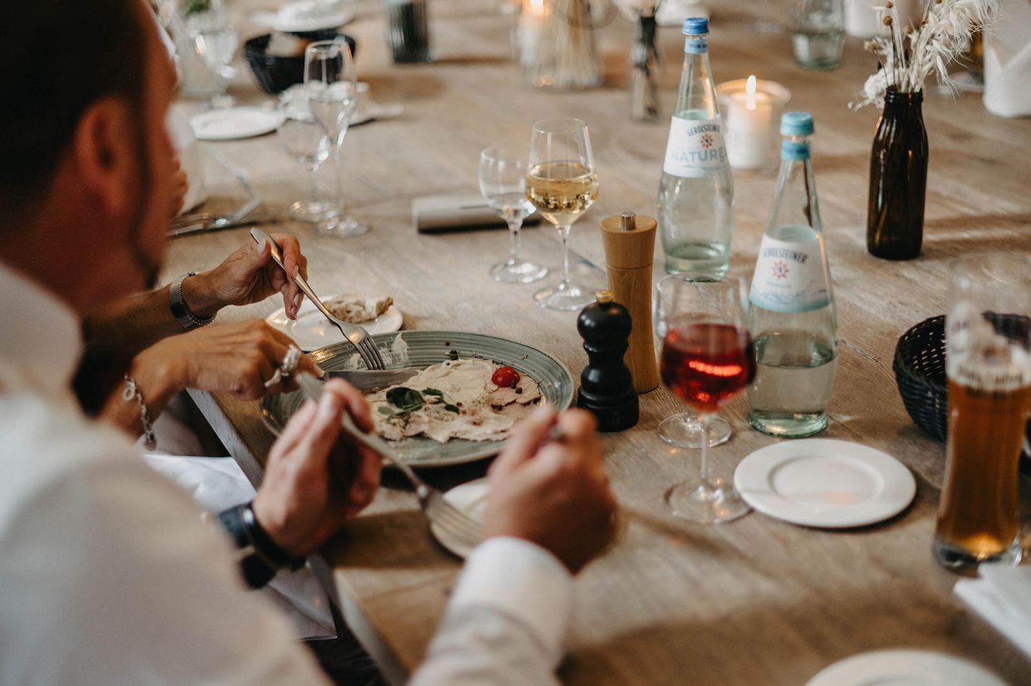 Close-up view of dining table settings with wine glasses and bottles during a meal.