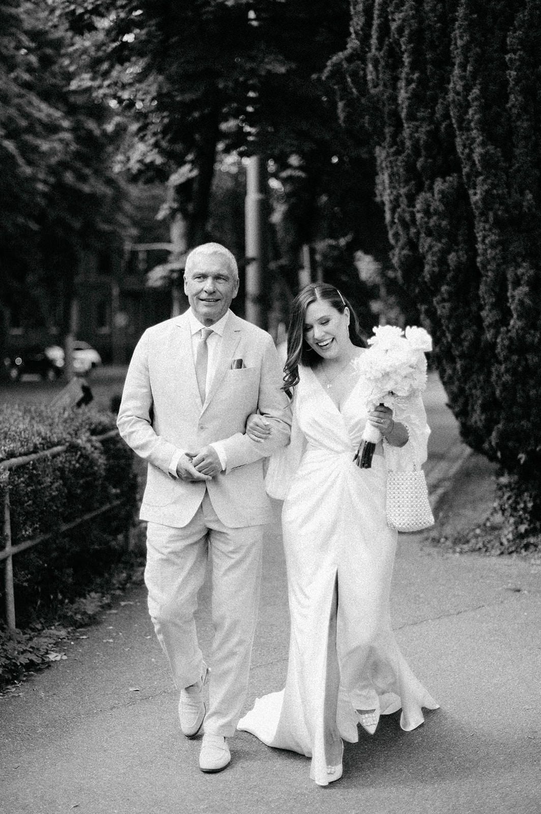 A black and white wedding photo of a couple walking outdoors, with the bride holding a bouquet.