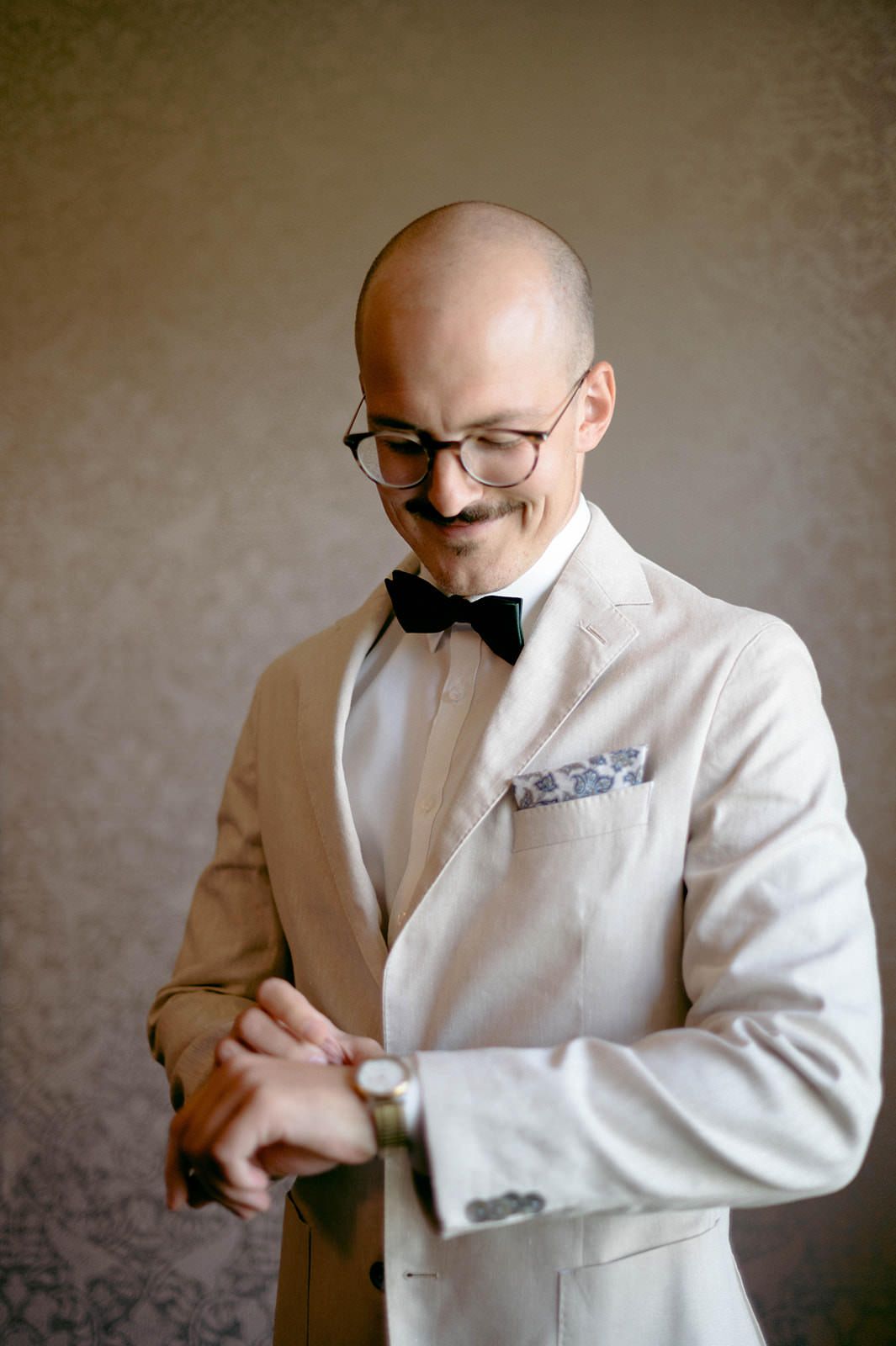A person in a white suit jacket adjusts their bow tie while getting ready in a series of candid shots.