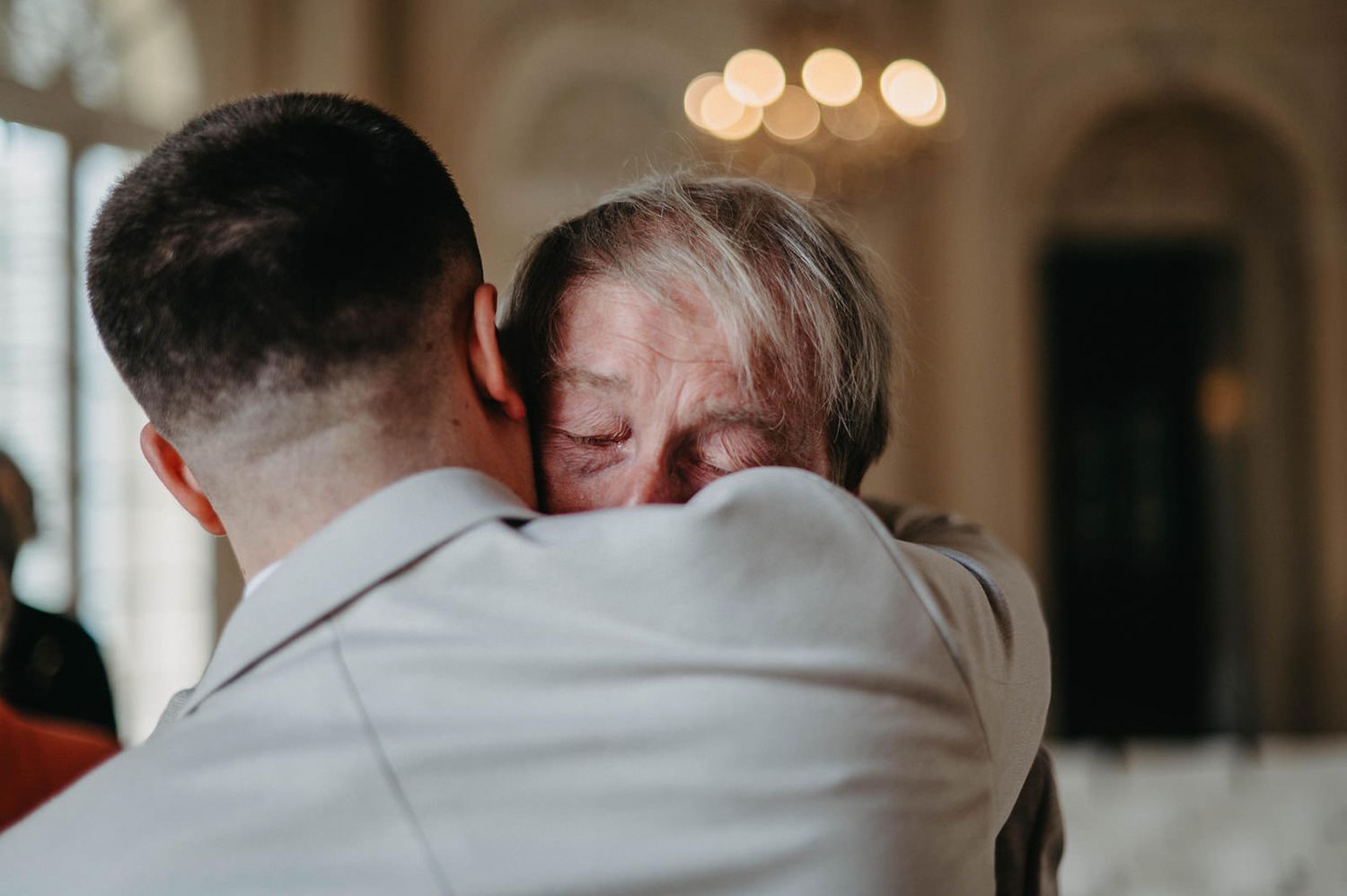 Intimate emotional embrace shared during wedding ceremony in elegant indoor setting with warm lighting.