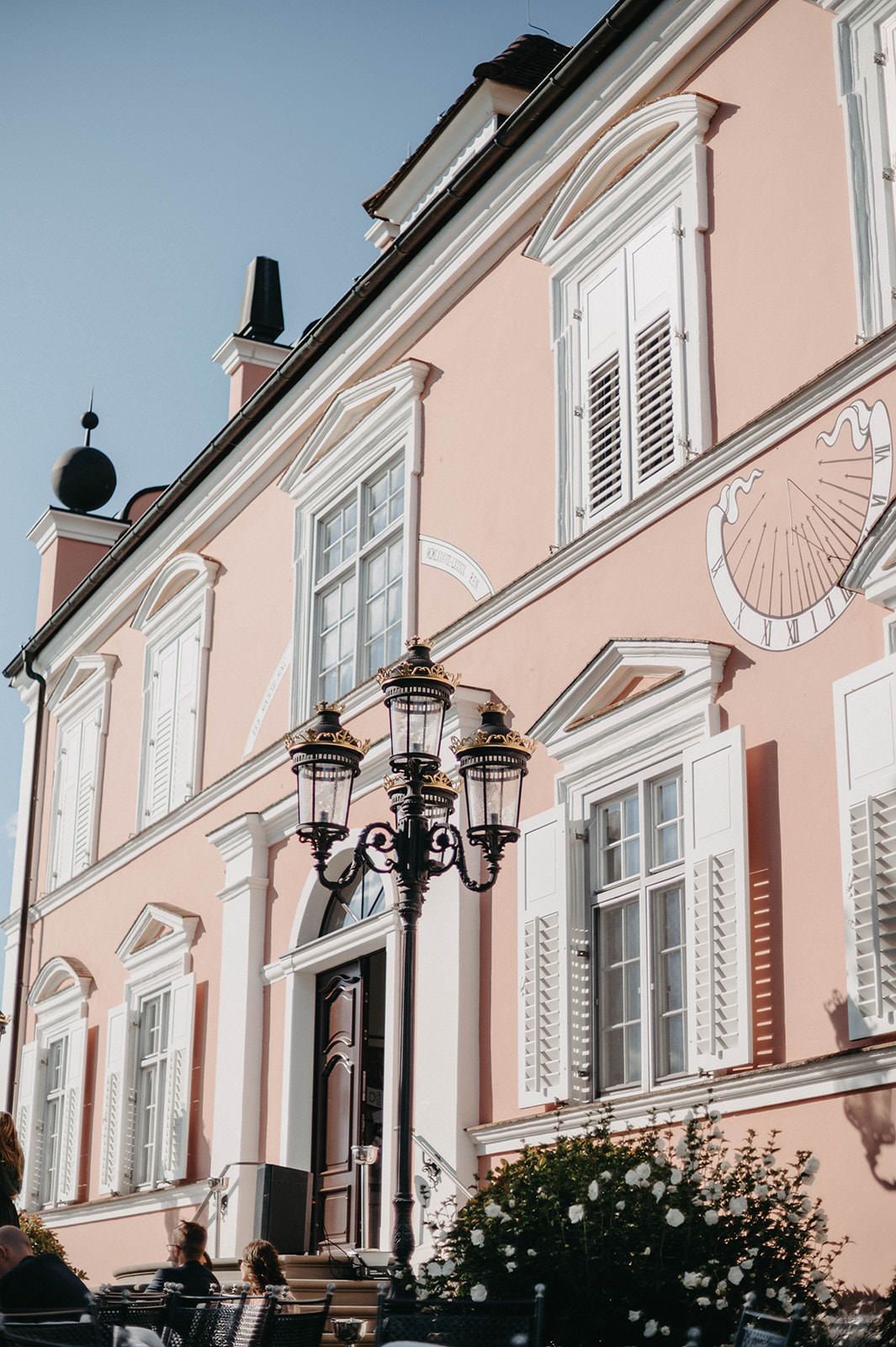 Elegant pink building facade with white trim and ornate black street lamps in European architectural style.