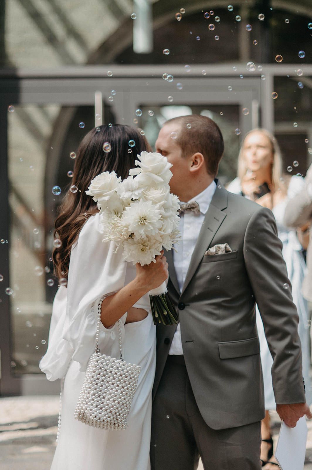 Newlyweds share a romantic moment surrounded by floating bubbles during outdoor wedding celebration.