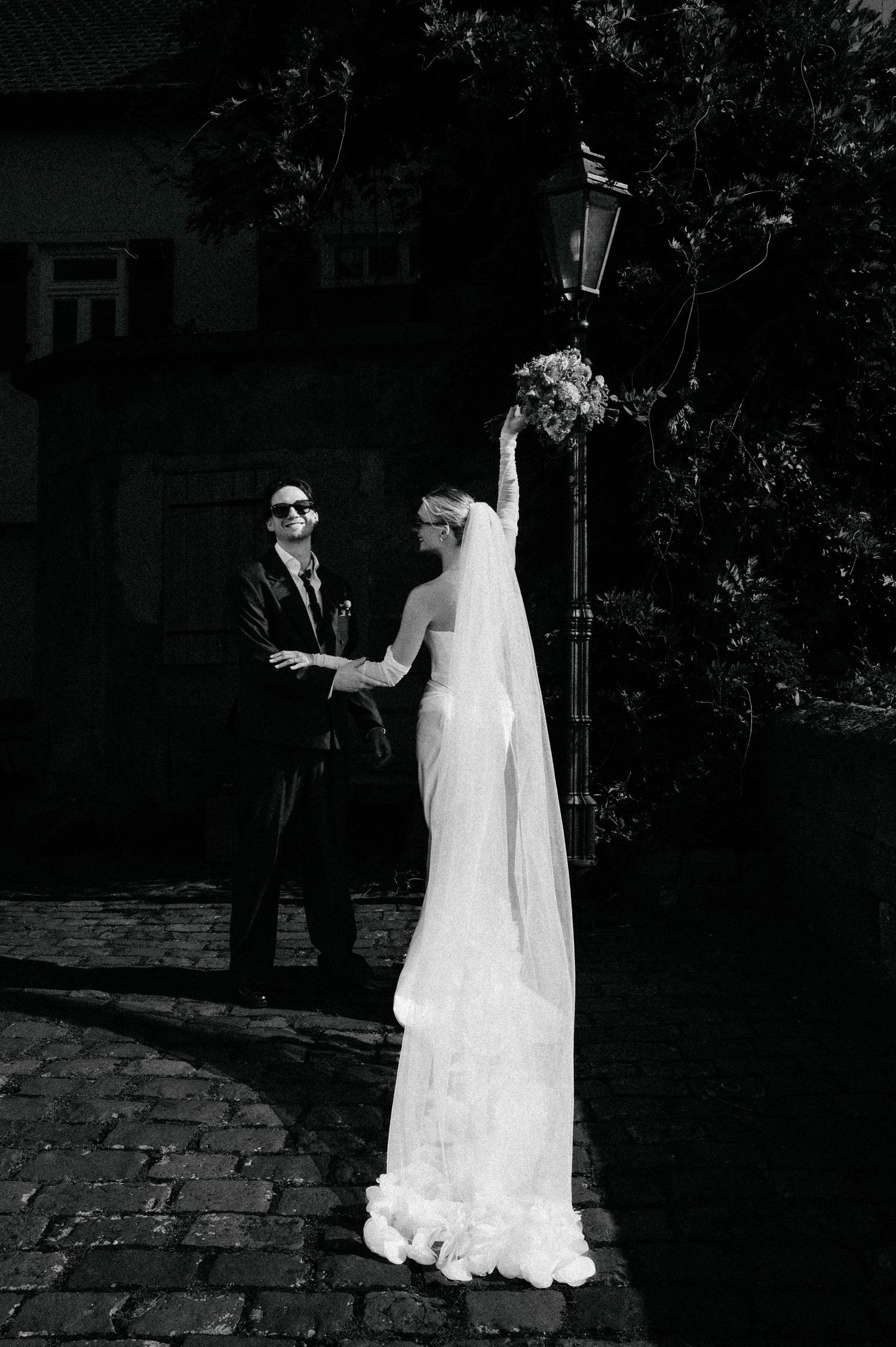 Black and white wedding portrait under vintage street lamp on cobblestone path.