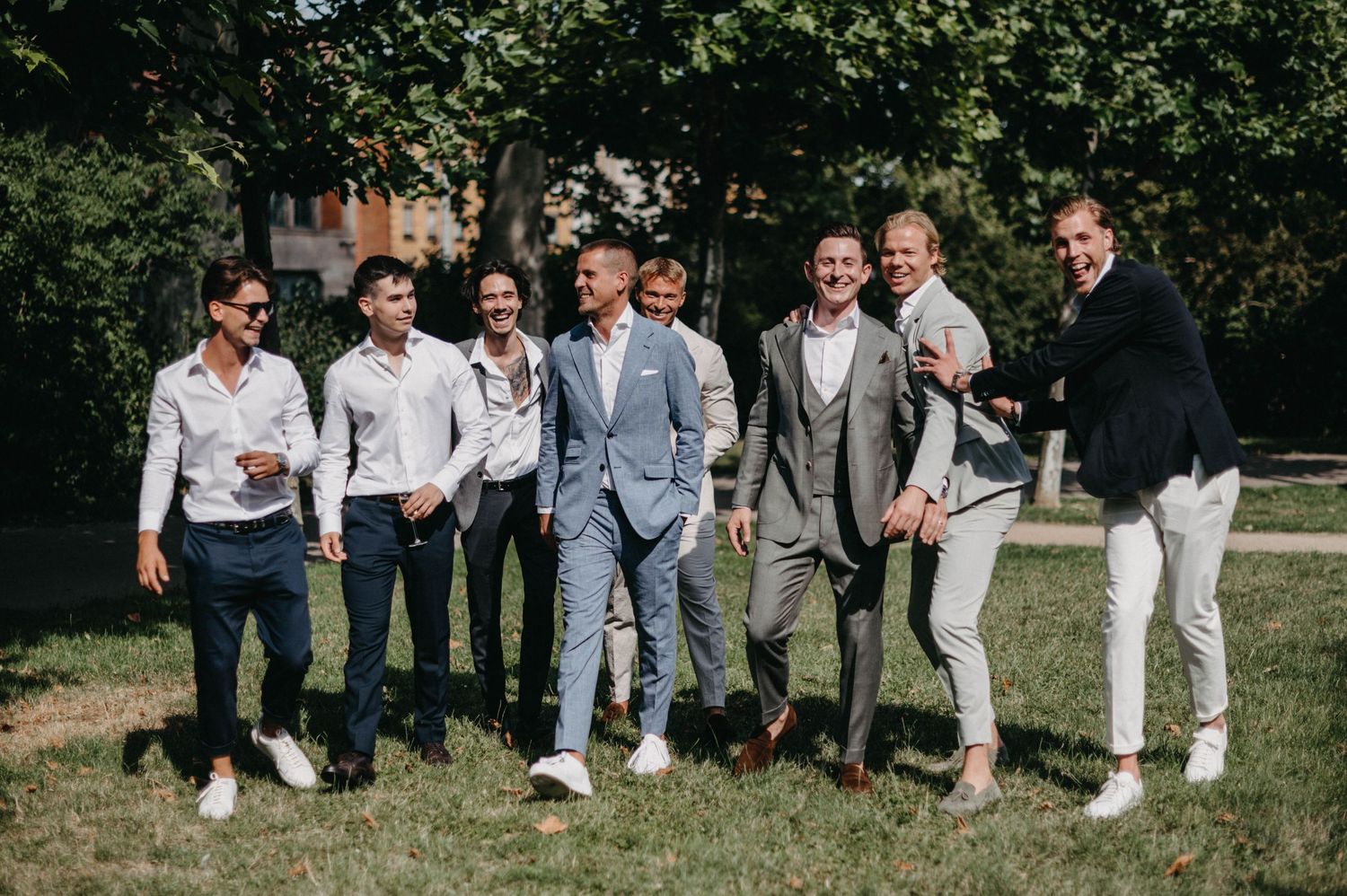 Group of wedding guests in casual attire posing on grass outdoors.