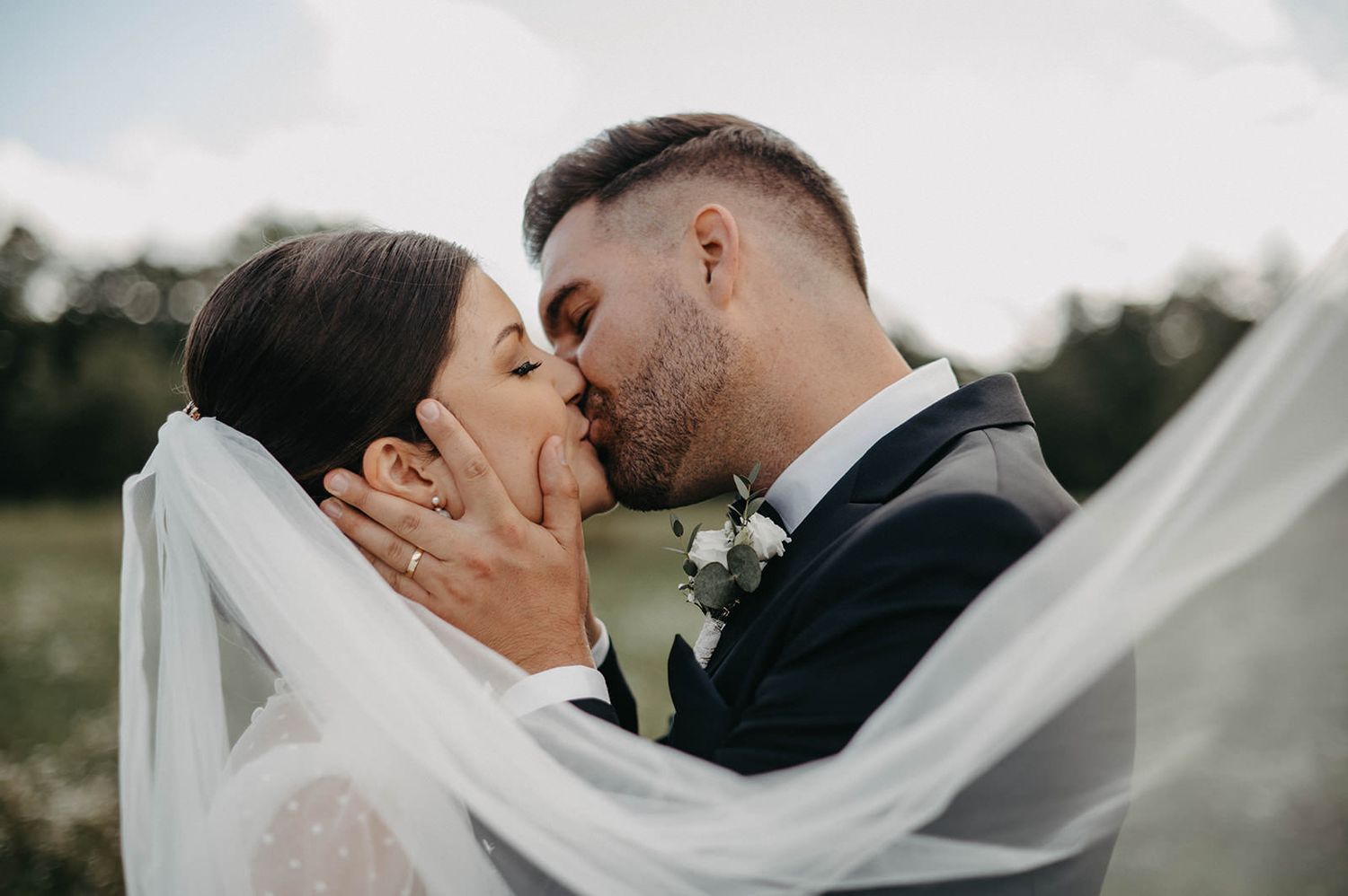 A romantic wedding couple shares an intimate moment as a long white veil flows in the breeze.