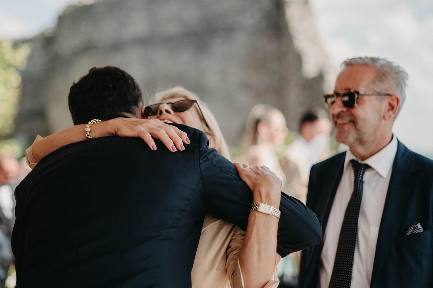 Emotional wedding moment as two people embrace during outdoor ceremony while guests look on.