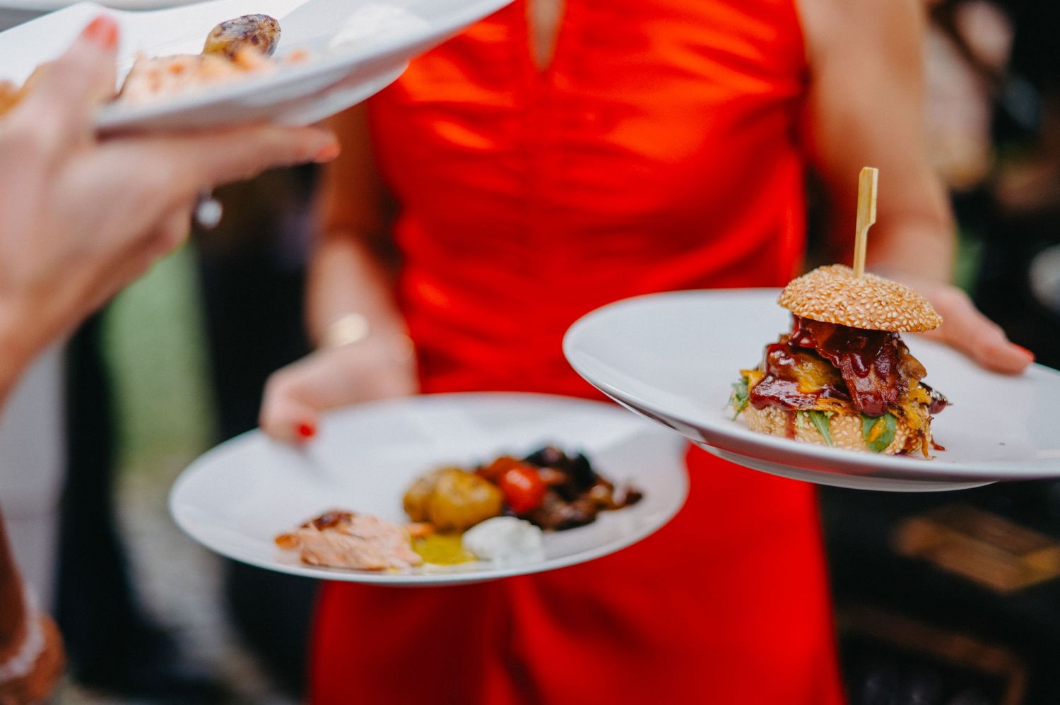 Hands in red sleeves serve elegant plated dishes at an upscale restaurant.