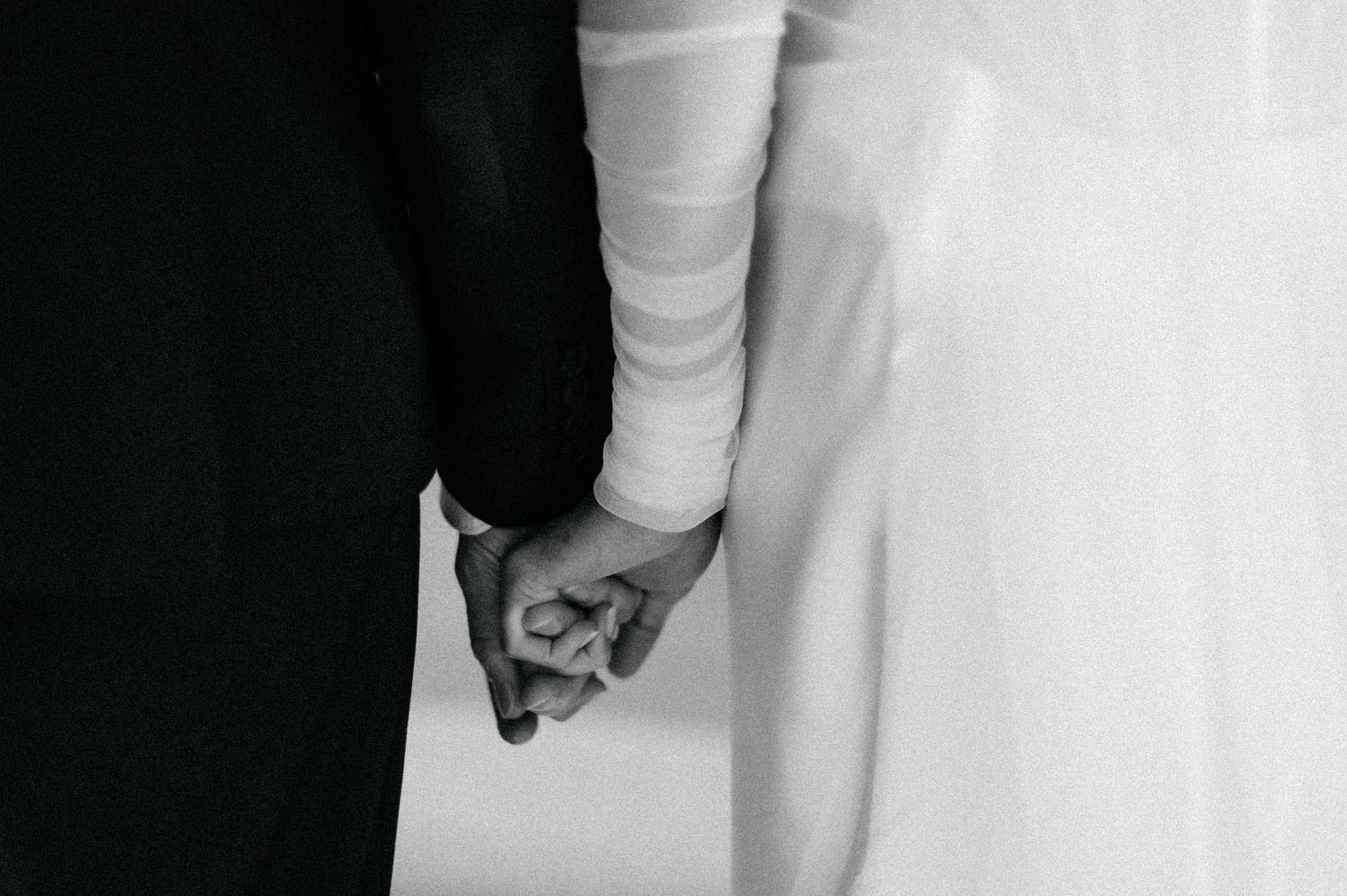A close-up view of a person wearing a white wedding dress and holding a bouquet with a blurred background.