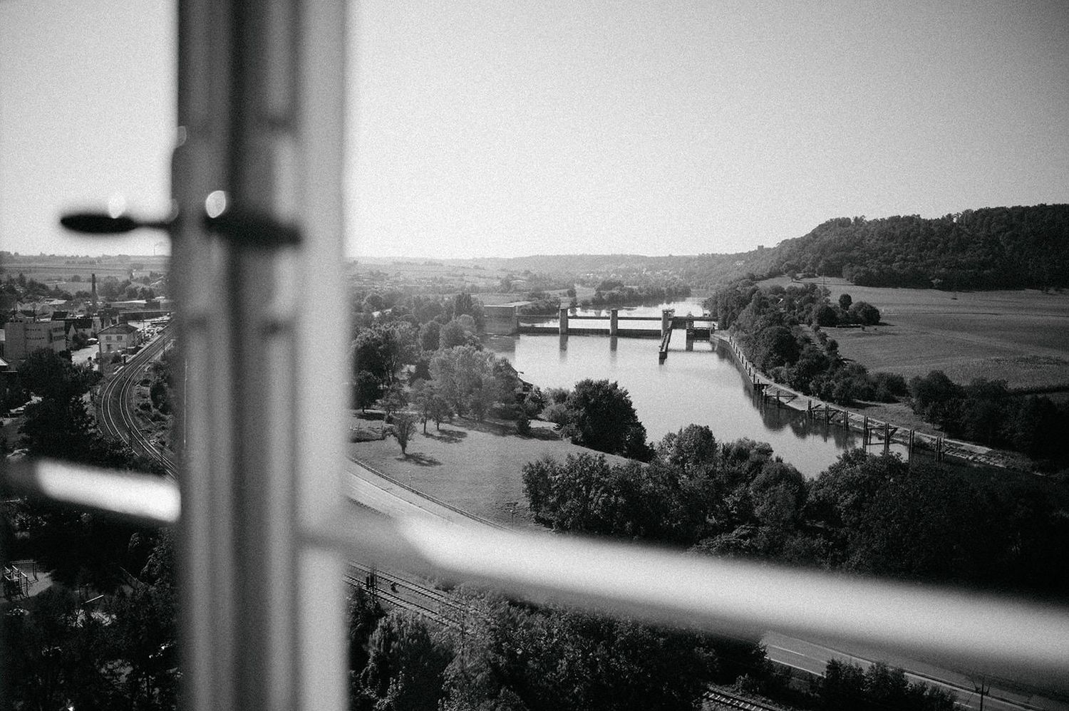 Black and white panoramic landscape view through a window showing rolling hills and a distant waterway.