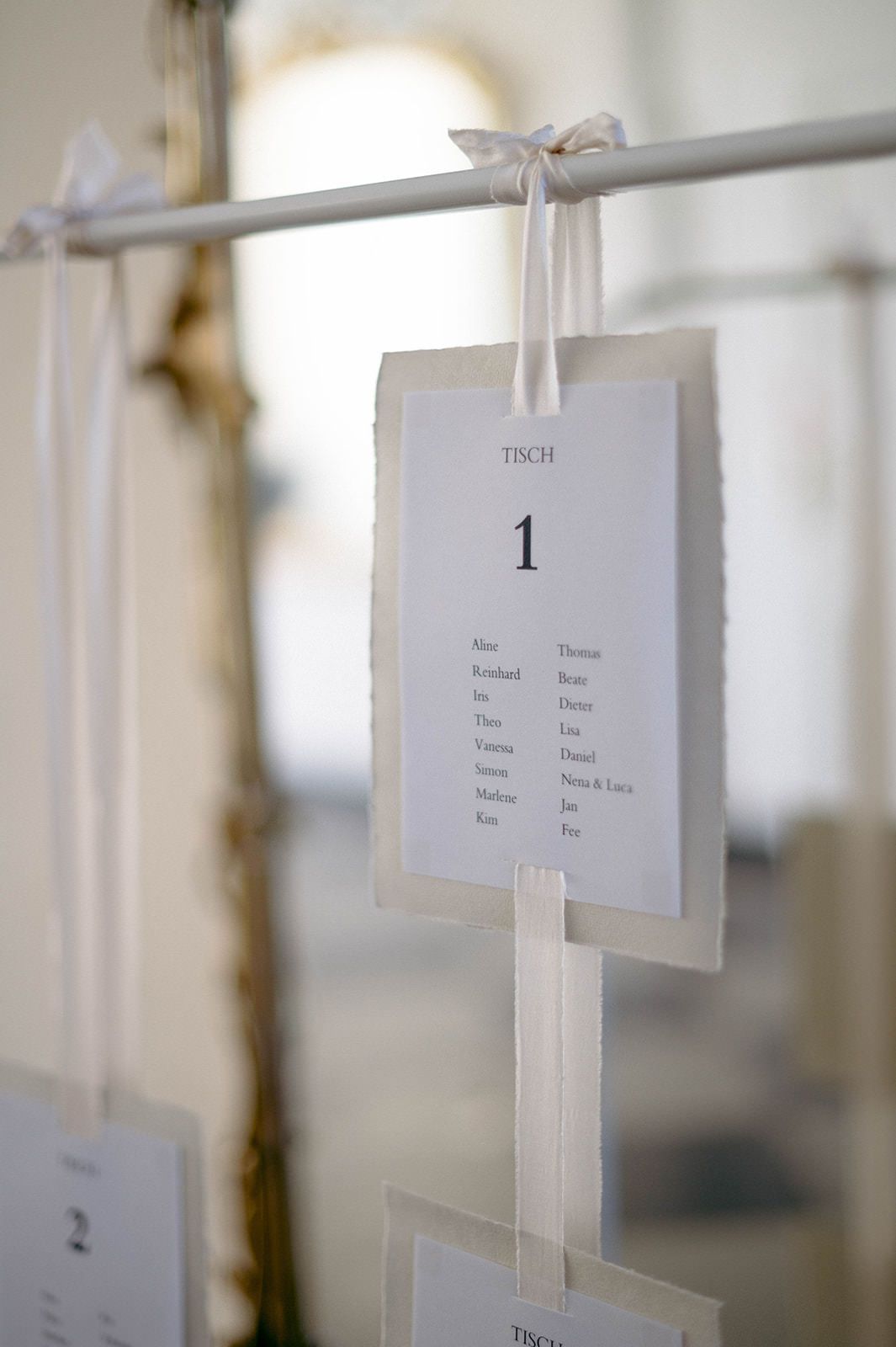 White paper cards with text hanging from strings create an elegant minimalist seating chart display at an event.
