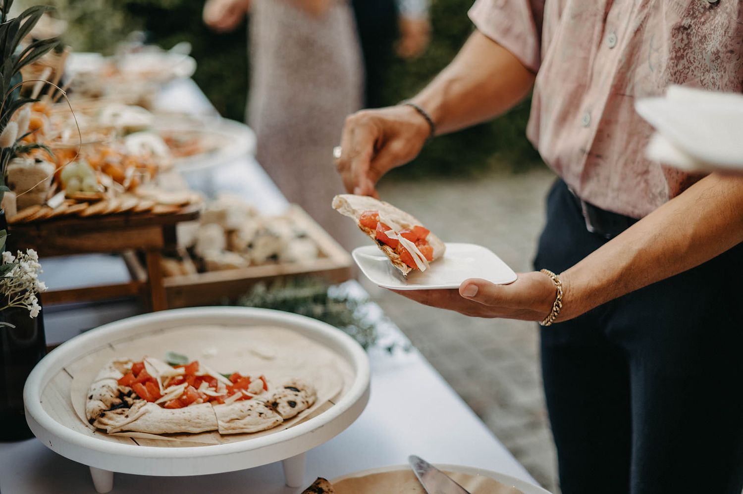Hands preparing and assembling traditional Mexican tacos with various toppings and fillings on white plates.