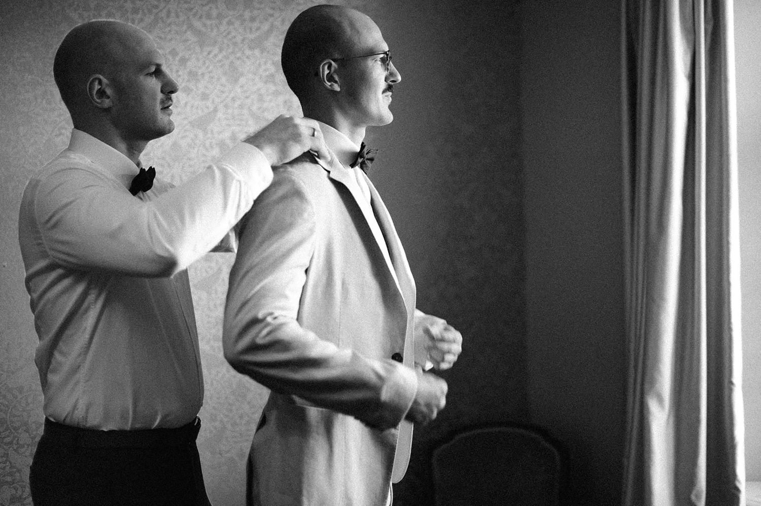 Black and white photo of groomsmen getting ready before a wedding ceremony, adjusting their formal attire.
