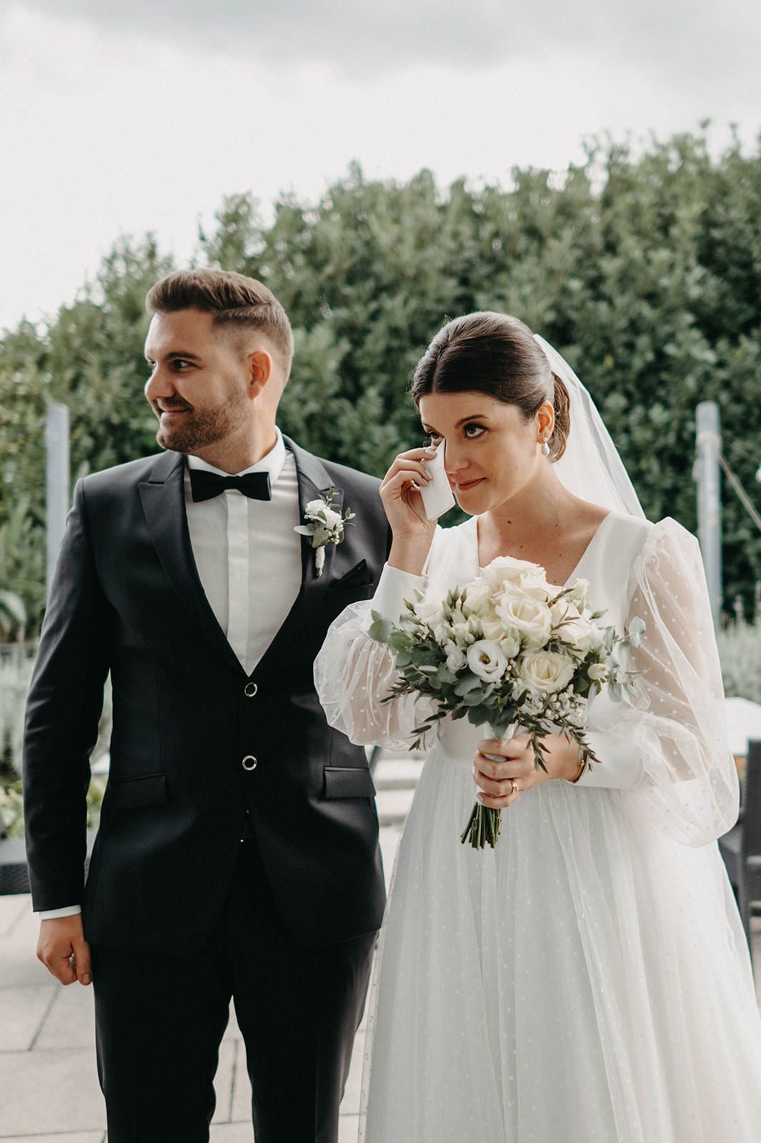 Wedding couple stands together in an elegant outdoor setting with white floral arrangements.