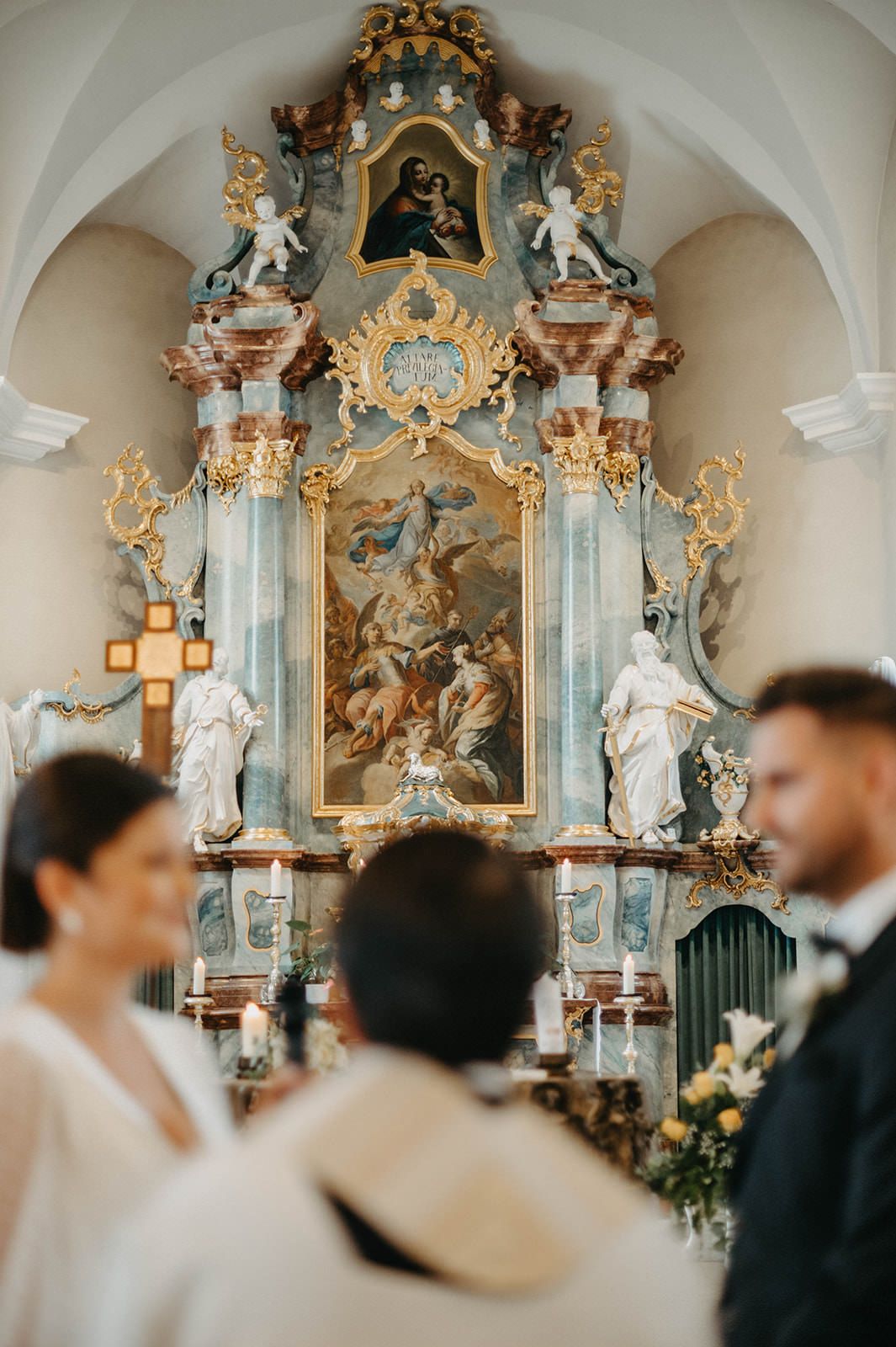 Ornate baroque church interior with gilded decorations and white statues during an elegant wedding ceremony.