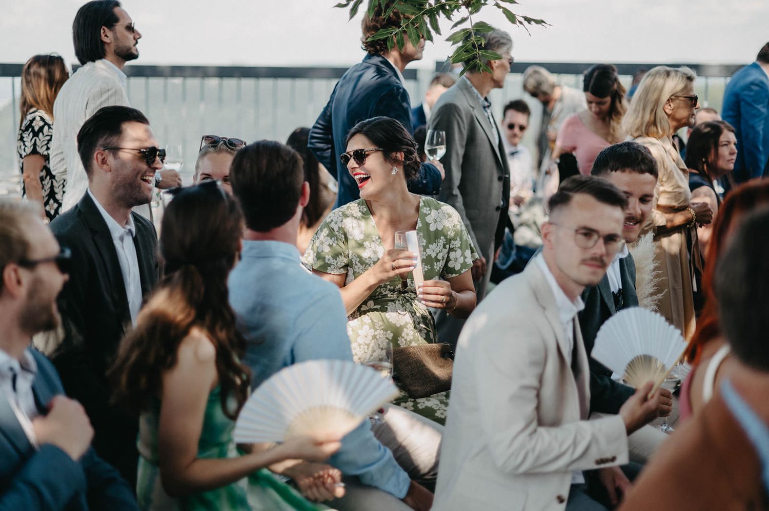 Wedding guests mingle and socialize during an outdoor cocktail reception on a sunny day.