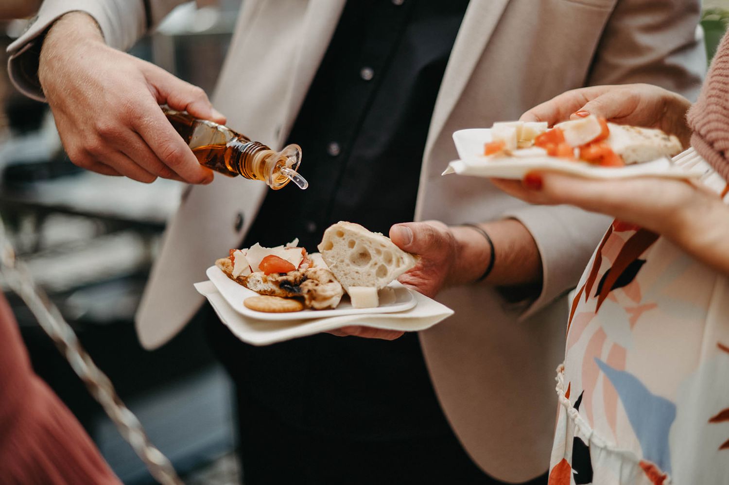 Multiple hands reaching for appetizers from elegant serving plates at an outdoor reception or party.