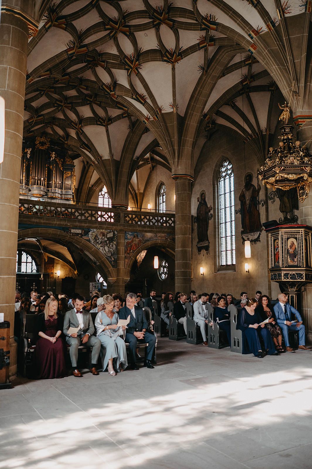 Gothic vaulted hall with ornate architecture filled with guests lined up along the walls during an event.