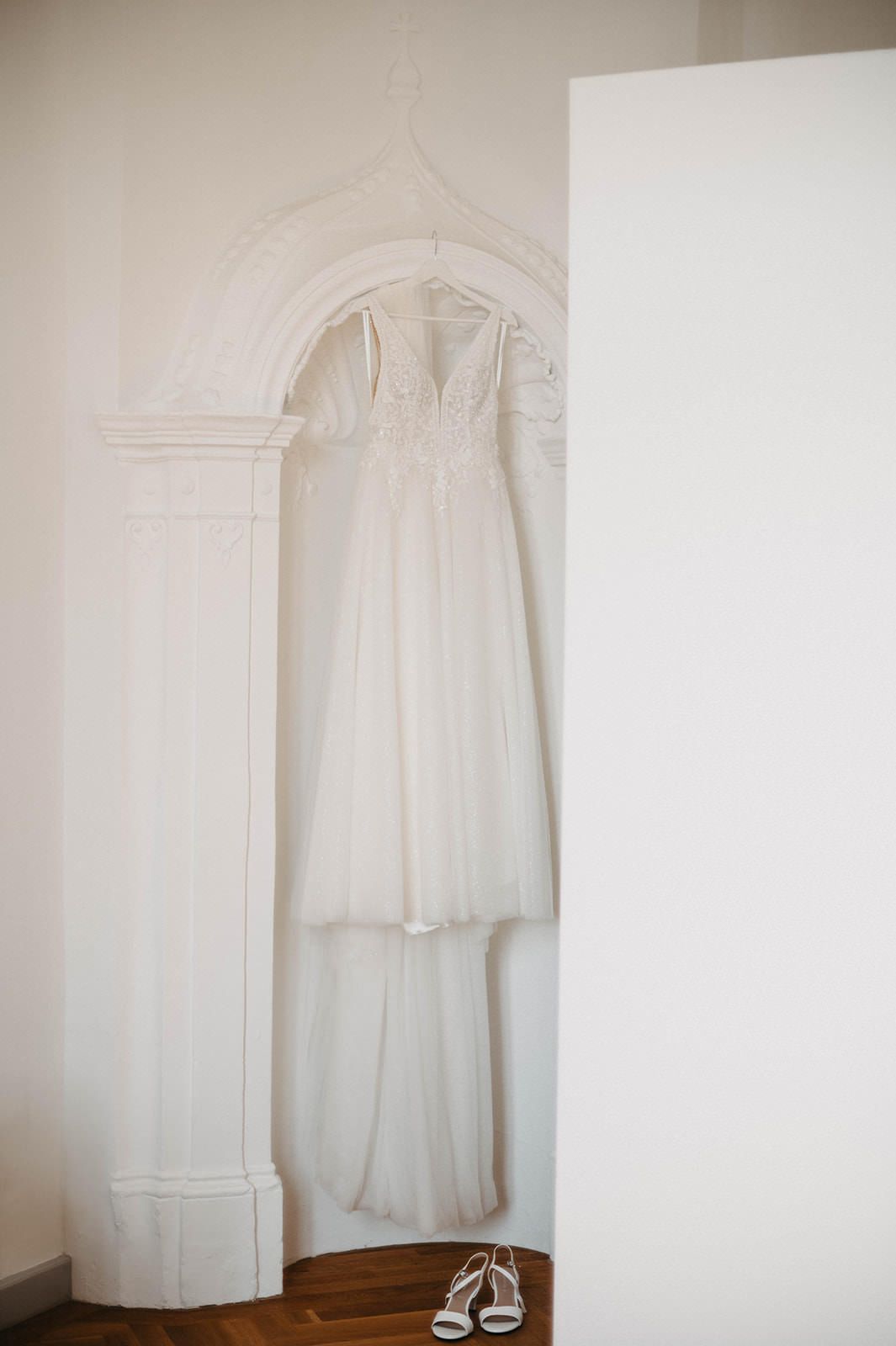 White wedding dress and silver shoes displayed in a minimalist corner setting with arched doorway detail.