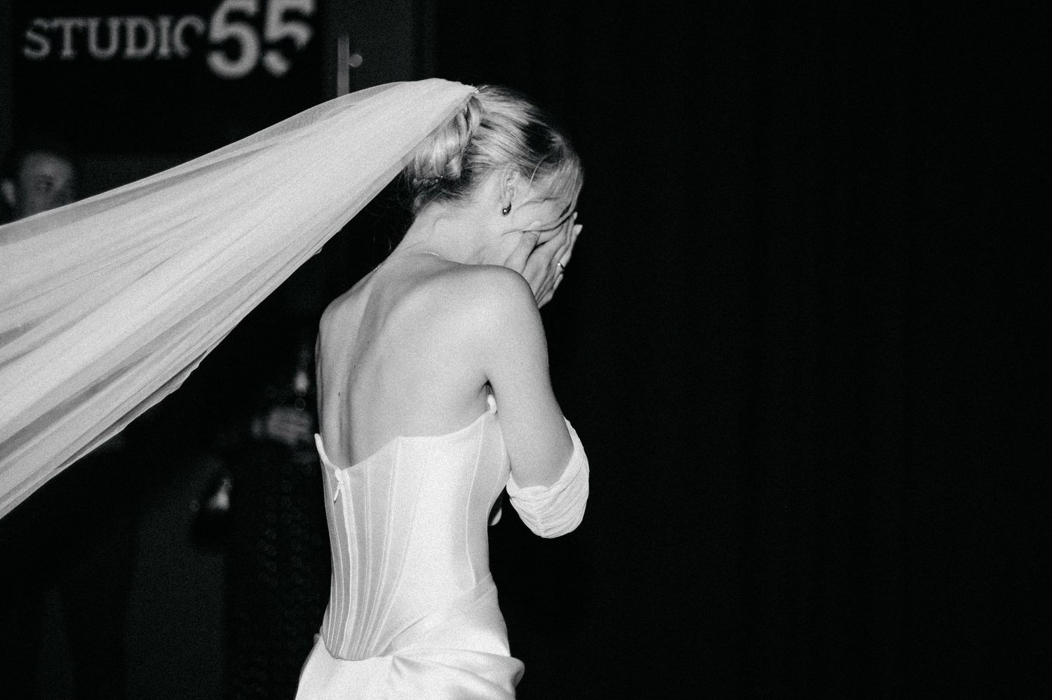 A bride in a white strapless wedding dress adjusts her flowing veil in a black and white photograph.