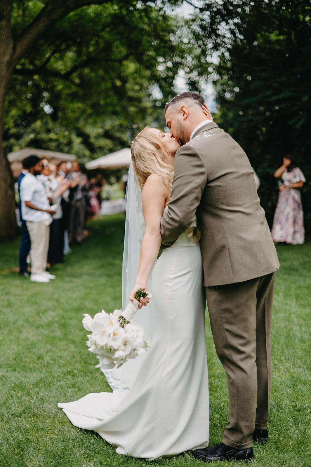 Romantic dip kiss sequence between newlyweds on a green lawn during outdoor wedding celebration.