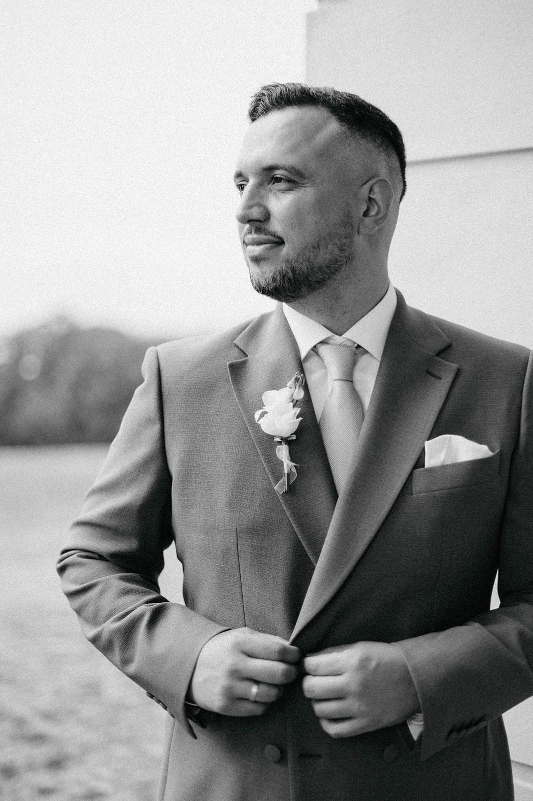 Close-up black and white photos of a groom adjusting his suit jacket and boutonniere.