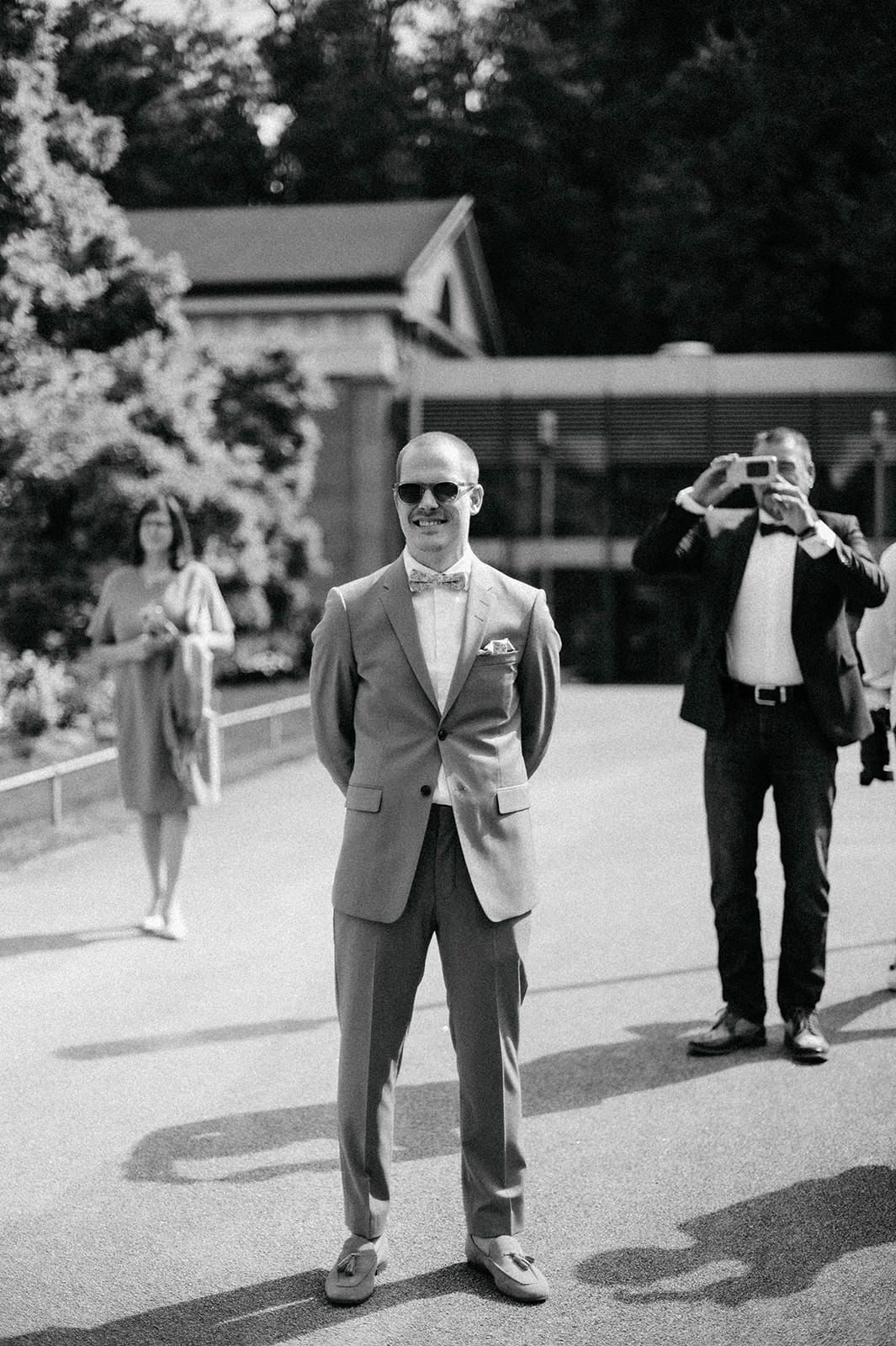 Black and white photograph of a formal outdoor event with people gathered on a paved walkway near a building.
