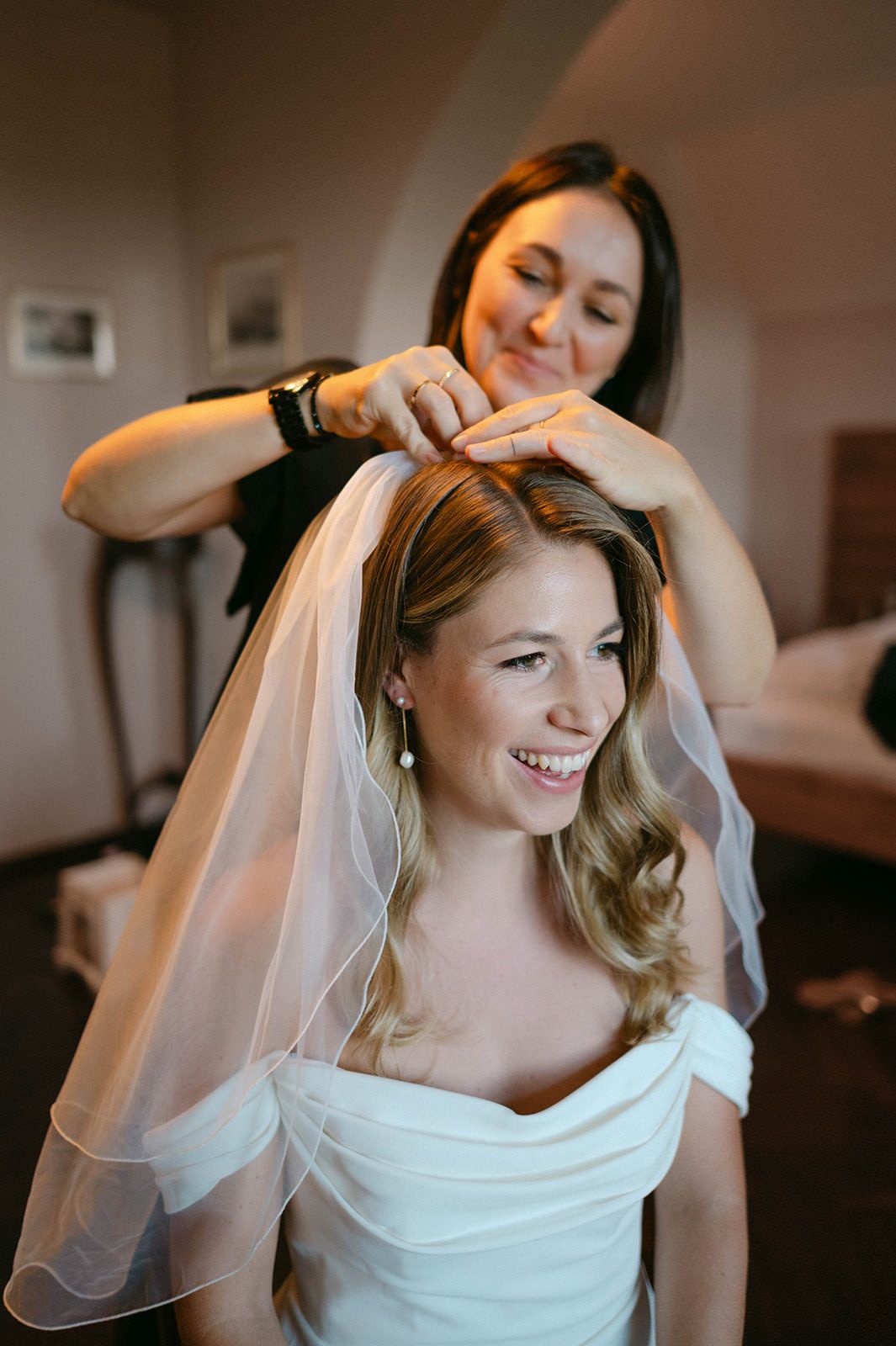 A bride has her veil carefully placed in her styled hair during wedding preparations.