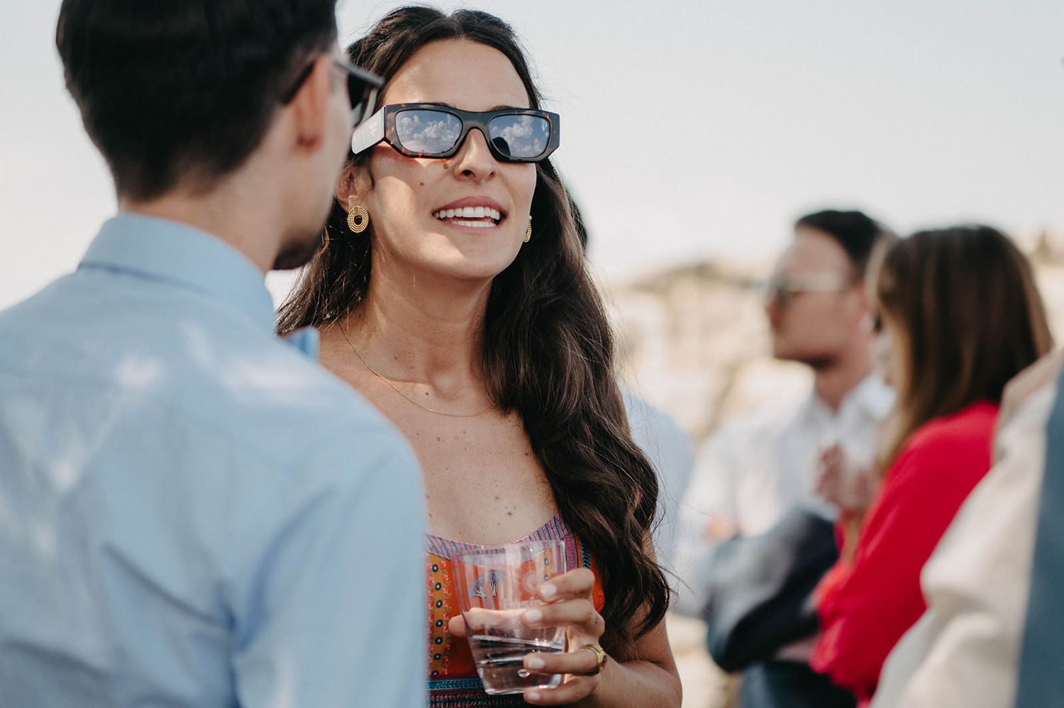 A group of people enjoying conversation and drinks at an outdoor social gathering at sunset.