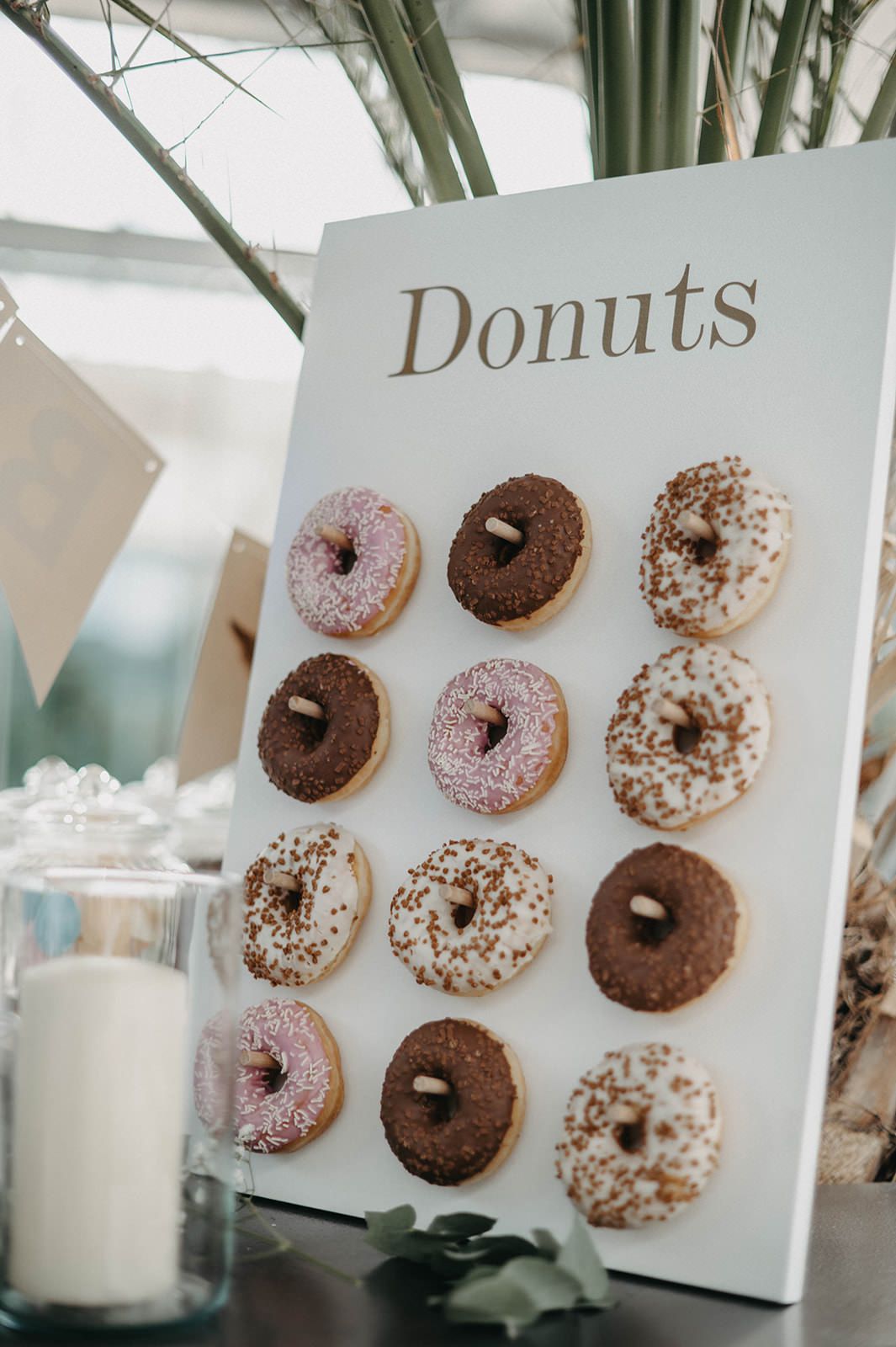 Assorted chocolate and vanilla frosted donuts displayed on white walls with a glass of milk.