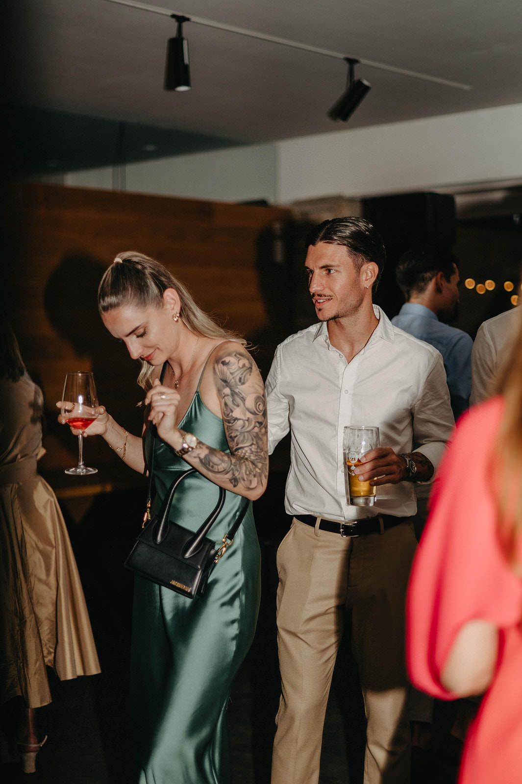Candid party scene with people laughing and drinking at a dimly lit indoor venue with wood paneling.