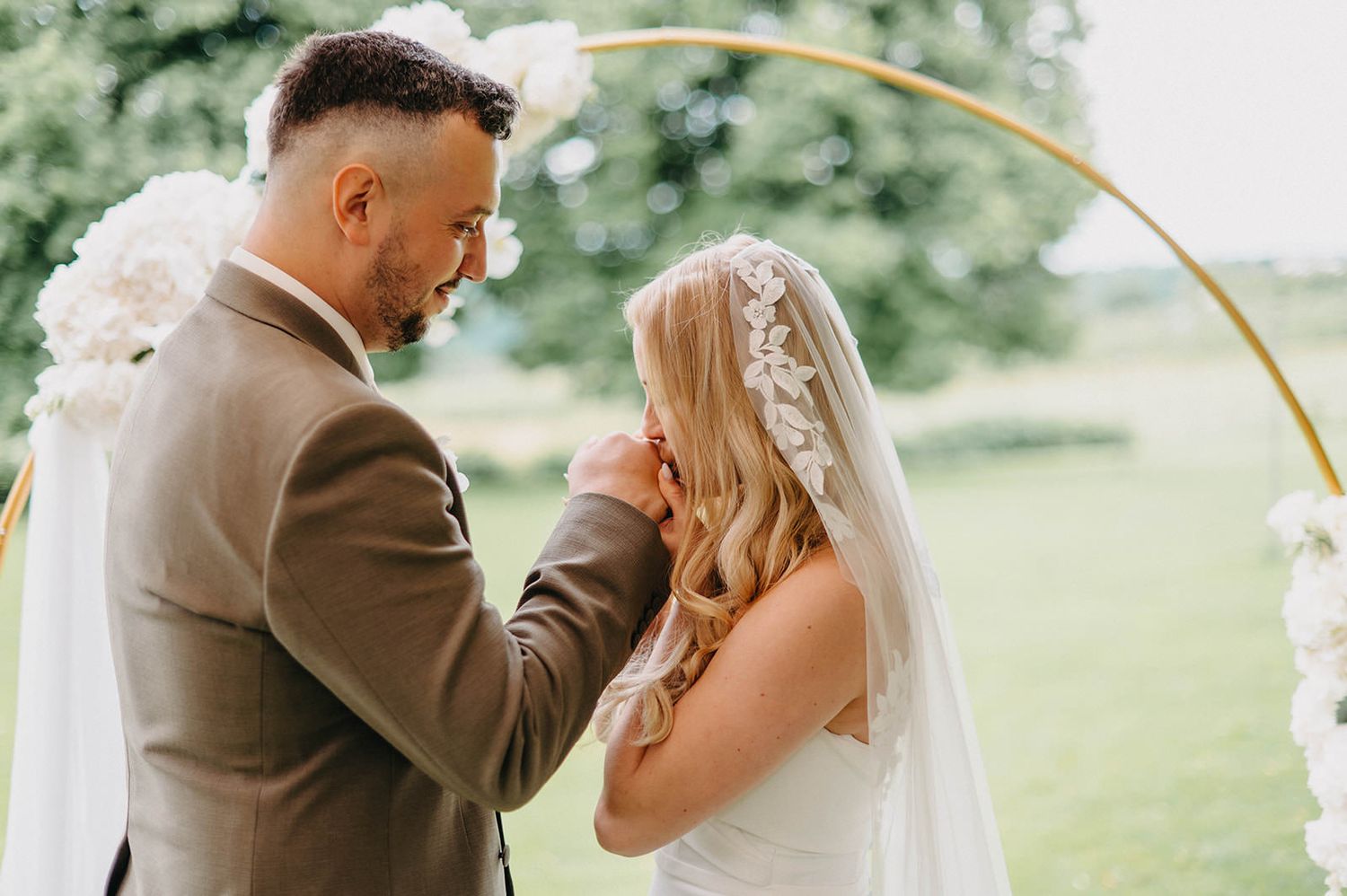 A bride and groom share an intimate moment during their outdoor wedding ceremony in a garden setting.