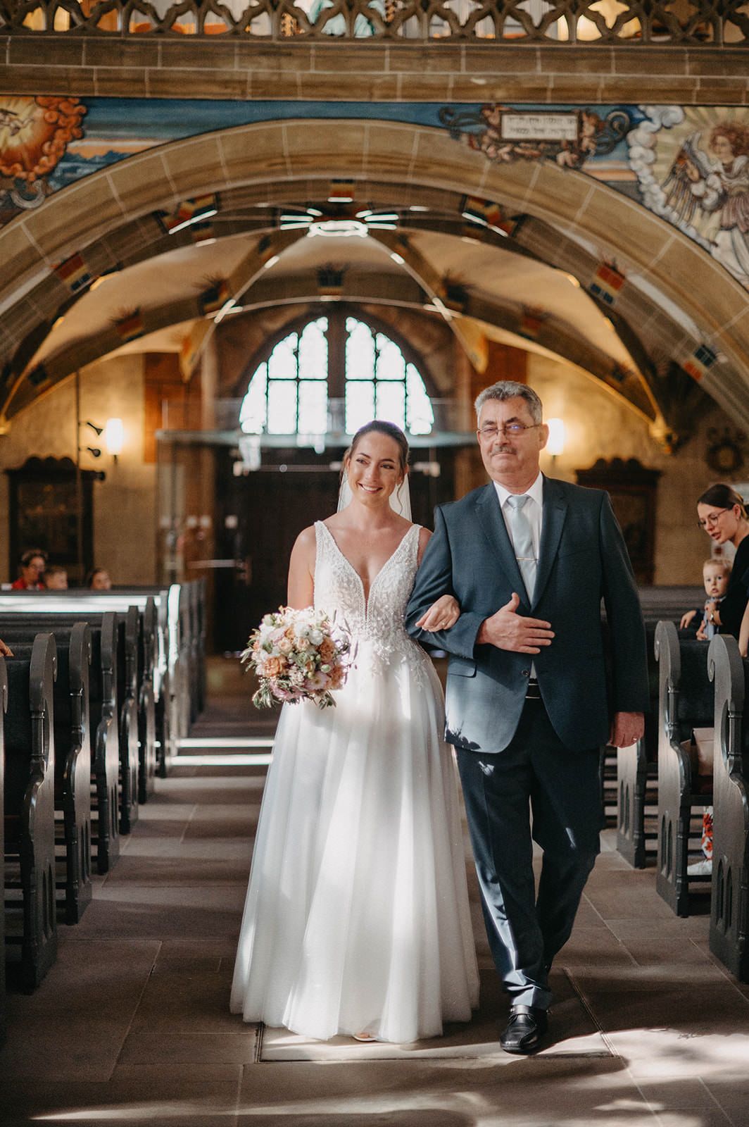 A couple walks down a grand stone church aisle with arched ceilings and ornate architectural details in natural light.