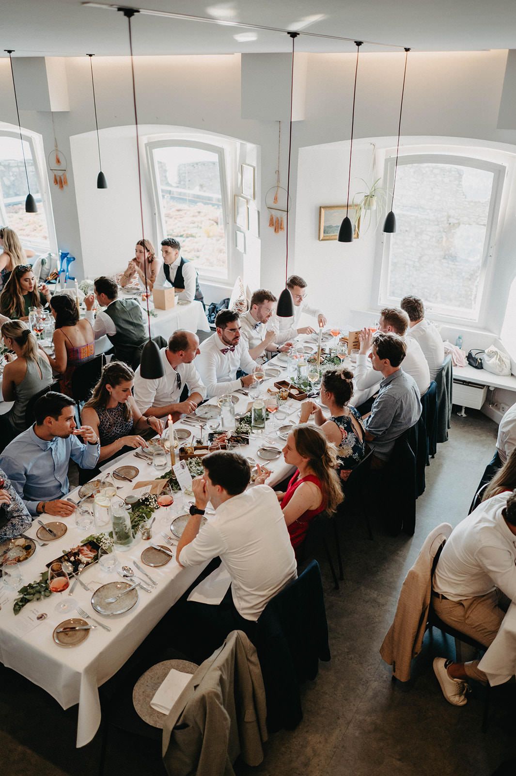 Wedding guests seated at long tables in a bright modern dining room during a reception celebration.