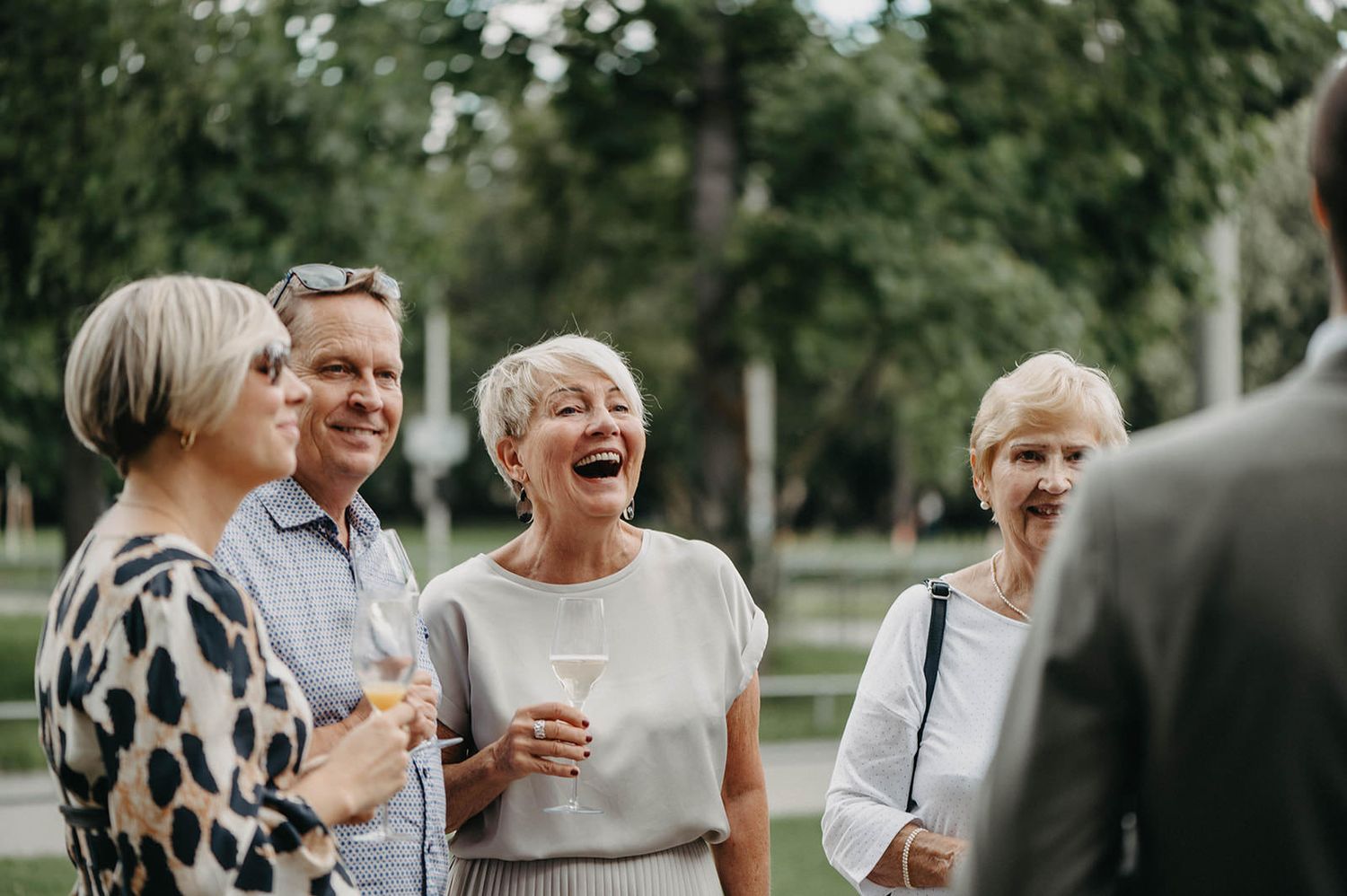 Group of friends sharing joyful laughter during outdoor gathering in a park setting.